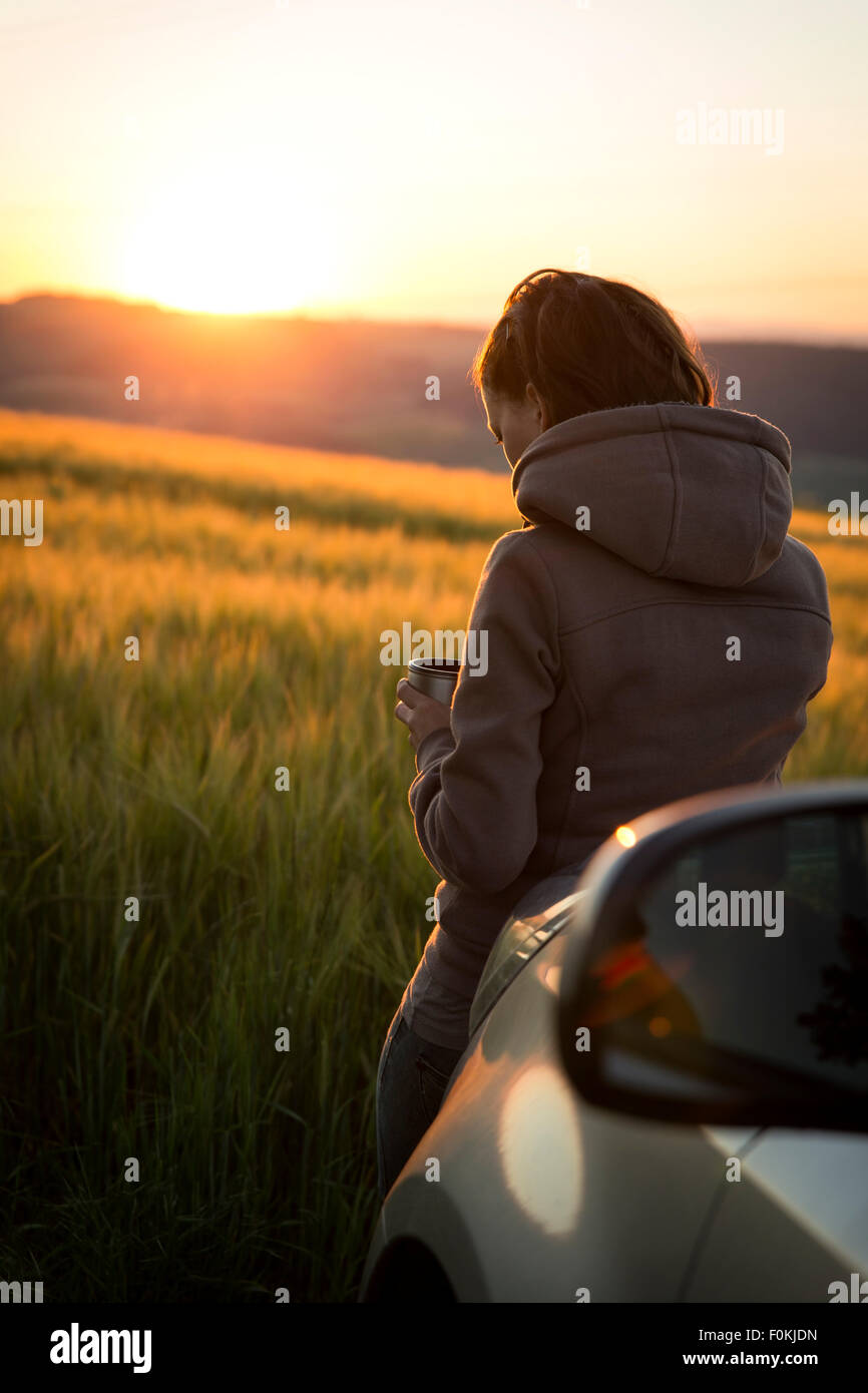 Germania, donna appoggiata sulla vettura davanti a un campo di sunrise Foto Stock