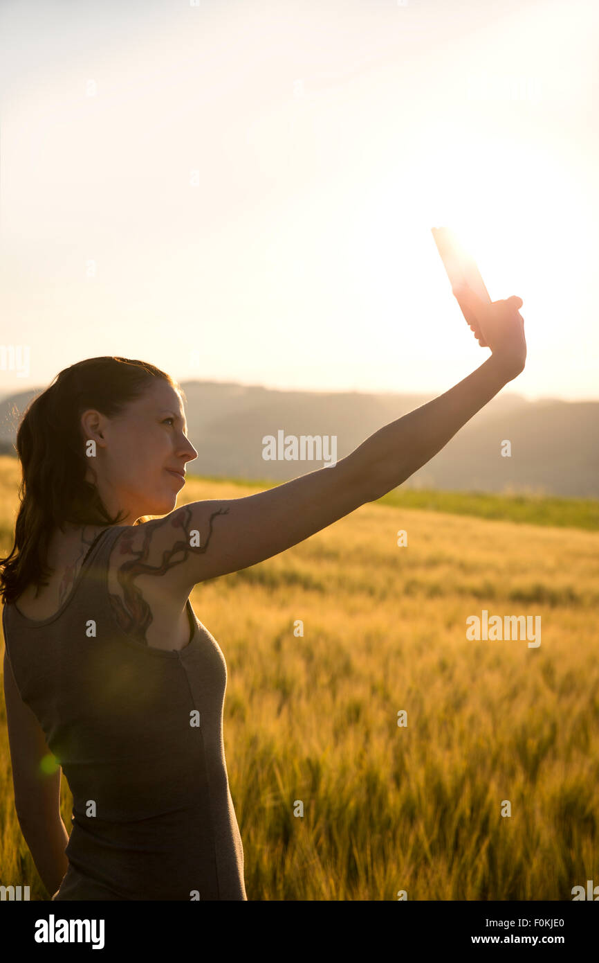 Germania, donna in piedi di fronte a un campo di sunrise prendendo un selfie con il suo smartphone Foto Stock