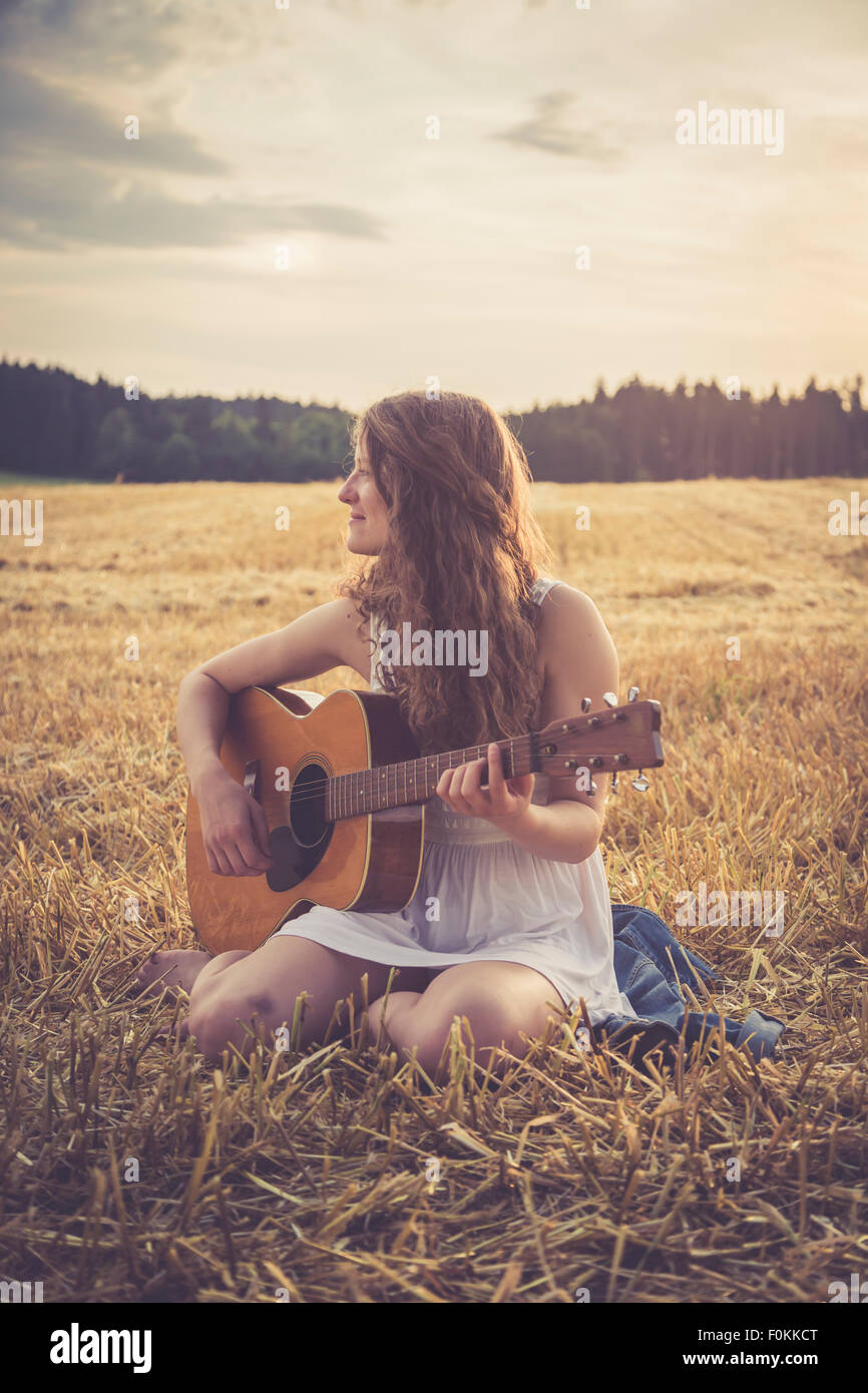 Giovane donna con la chitarra seduta sul campo di orzo di sera Foto stock -  Alamy