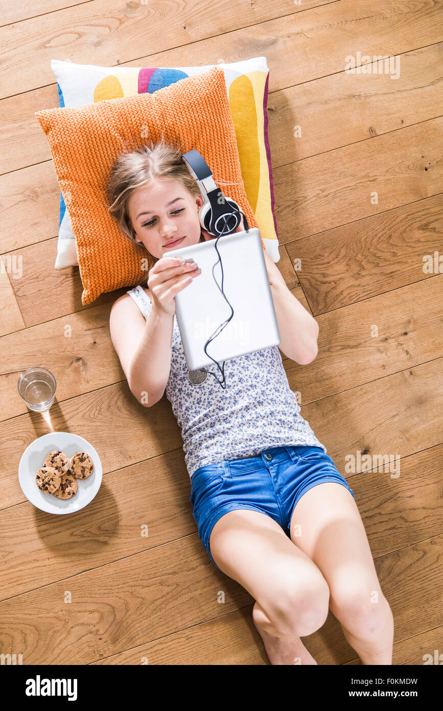 Ragazza adolescente giacente sul piano ascoltando la musica dalla tavoletta digitale Foto Stock