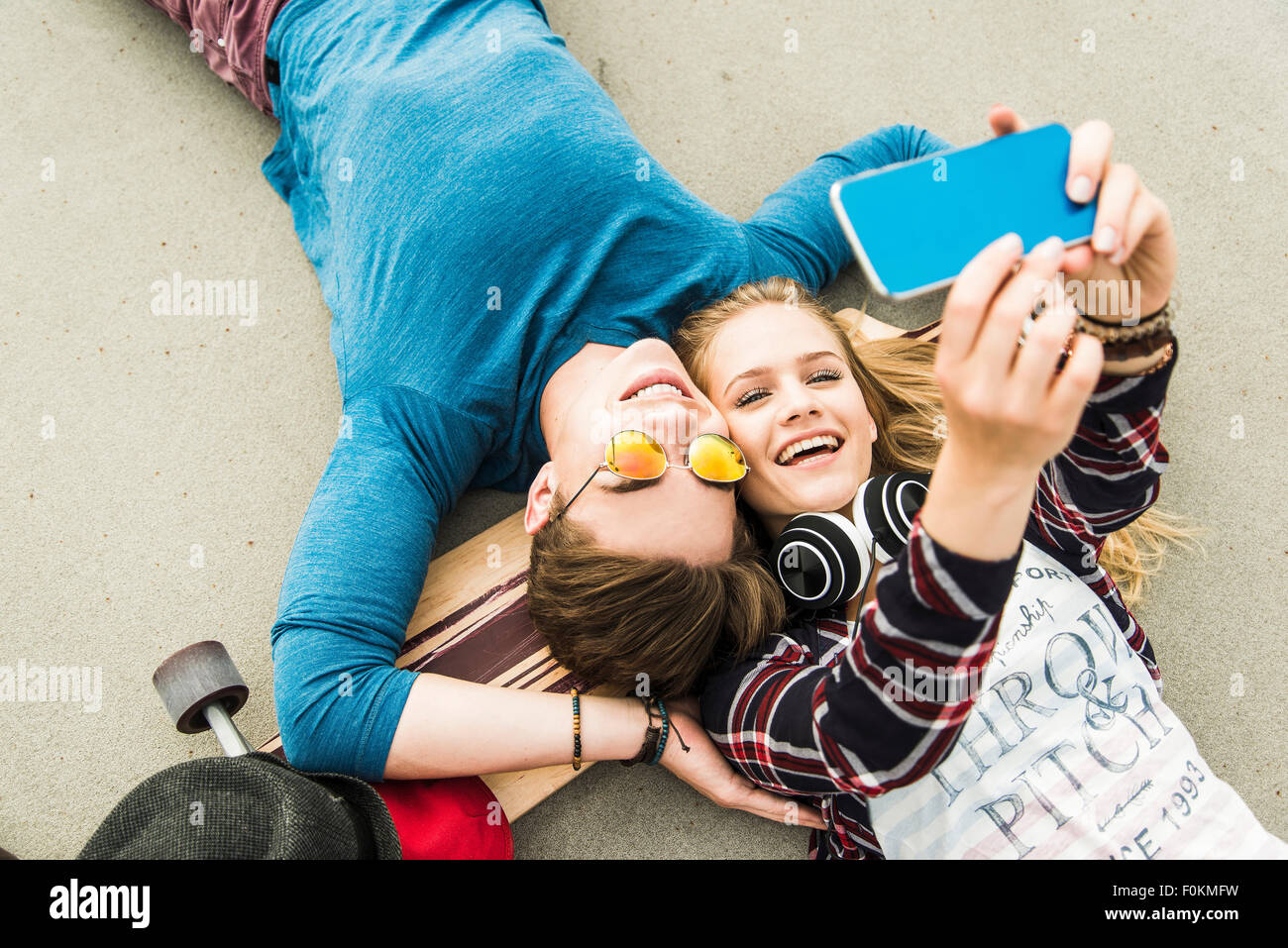 Felice coppia giovane disteso sul terreno con lo skateboard guardando al telefono cellulare Foto Stock