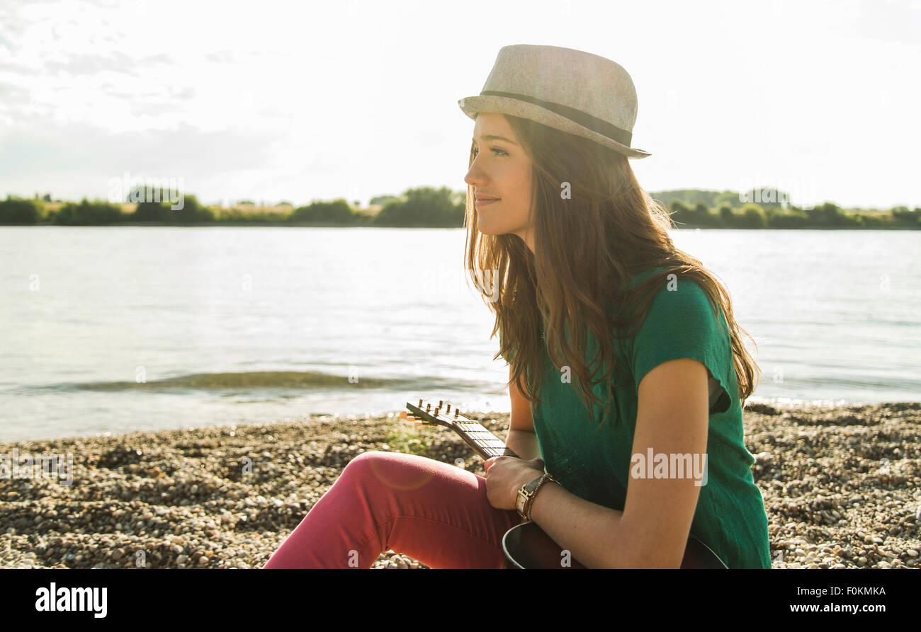 Giovane donna con la chitarra seduto da riverside Foto Stock