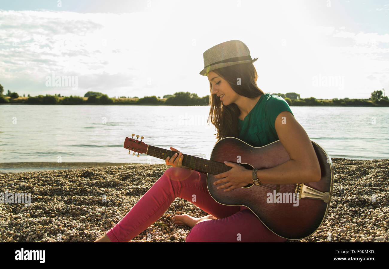 Giovane donna a suonare la chitarra da riverside Foto Stock
