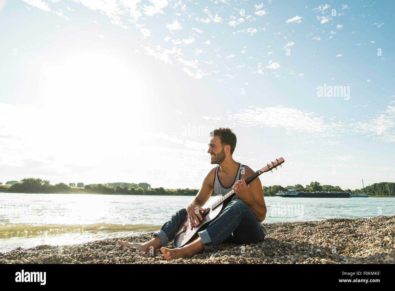 Giovane uomo con la chitarra seduto da riverside Foto Stock