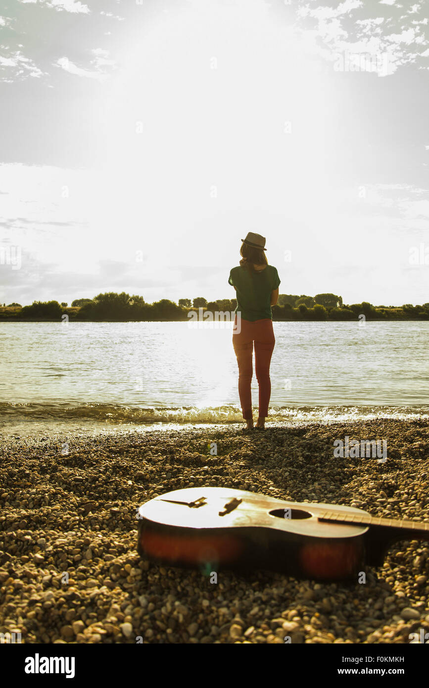Giovane donna in piedi dalla riva con la chitarra in primo piano Foto Stock