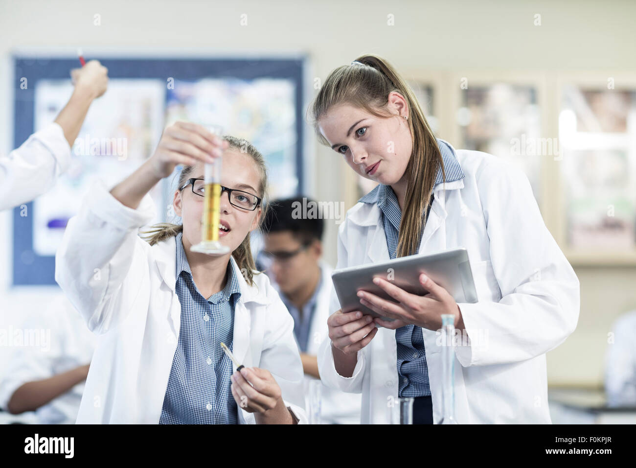 Due studentesse in chimica classe con liquido e tavoletta digitale Foto Stock