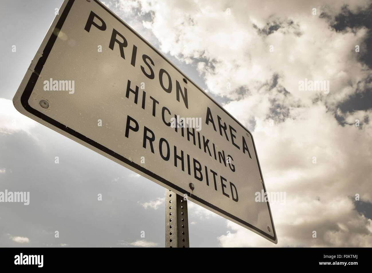 Lettura del segno "Carcere, autostop vietata " sta in piedi di fronte ad una prigione/penitenziario nel paesaggio del deserto. Foto Stock