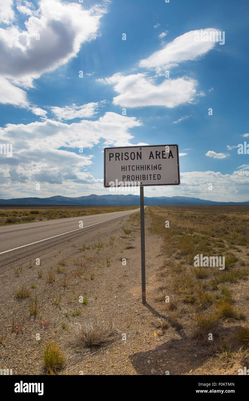 Lettura del segno "Carcere, autostop vietata " sta in piedi di fronte ad una prigione/penitenziario nel deserto paesaggio Foto Stock