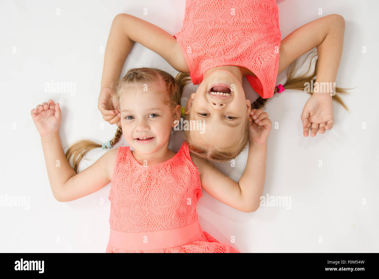 Due ragazze sorelle della biancheria stessa giacciono su una superficie bianca accanto a un testa a testa guarda le foto e sorridente Foto Stock