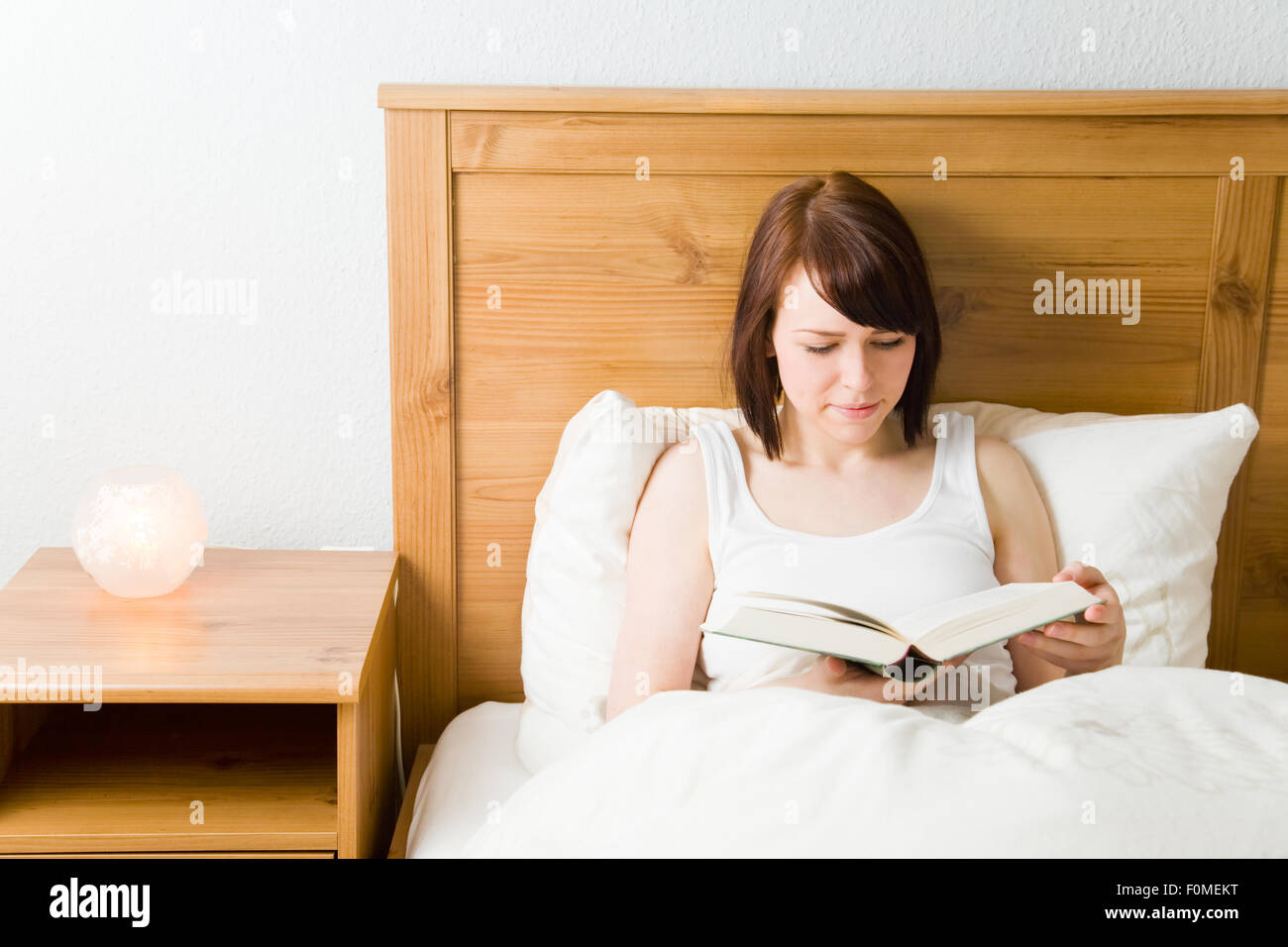 Giovane donna la lettura di un romanzo nel suo letto Foto Stock