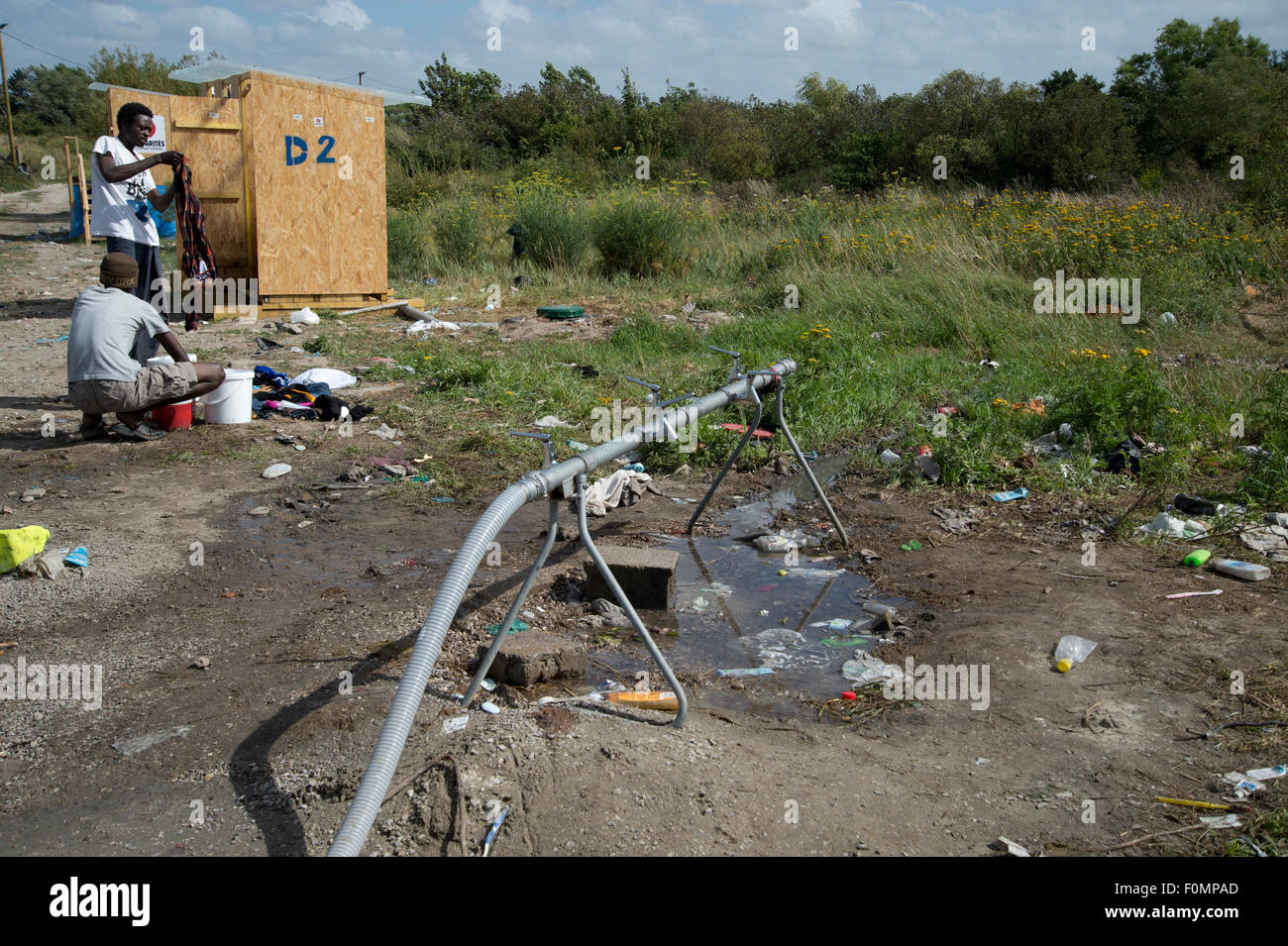 La migrazione a Calais. La giungla campo di fortuna.Due uomini lavare i vestiti da un rubinetto di stand. Foto Stock