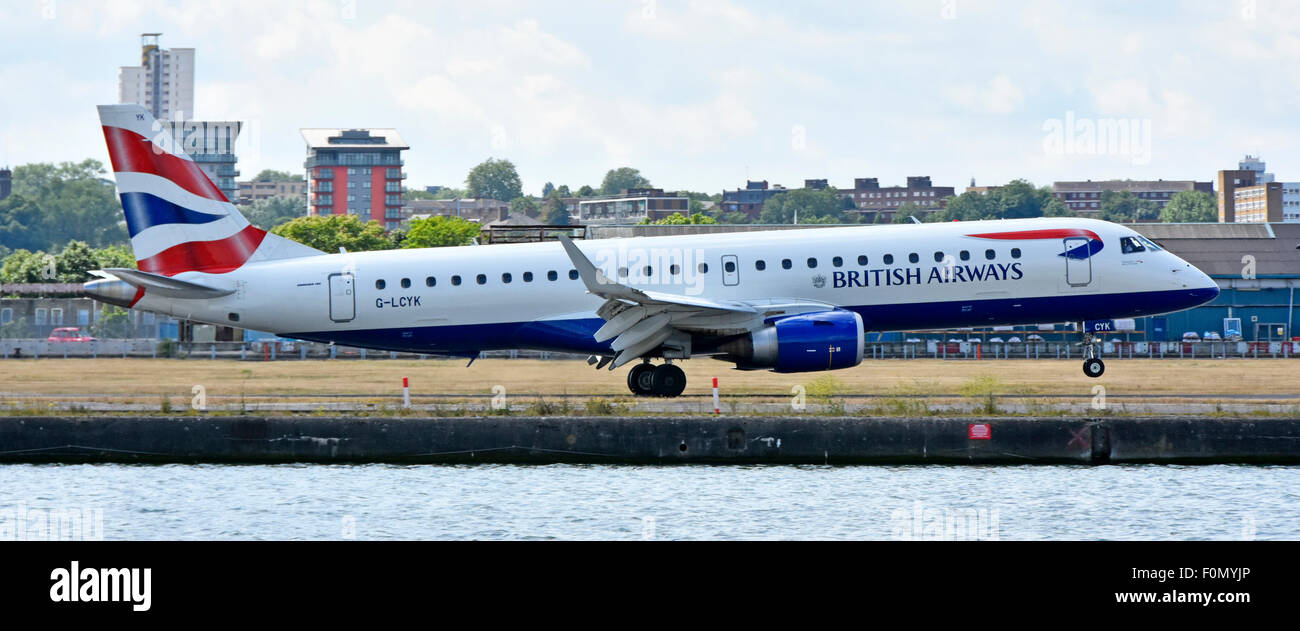 British Airways Cityflyer Embraer 190 G-LCYK sbarco & touchdown all'Aeroporto di London City accanto al vecchio dock acque in East London Docklands Newham Regno Unito Foto Stock