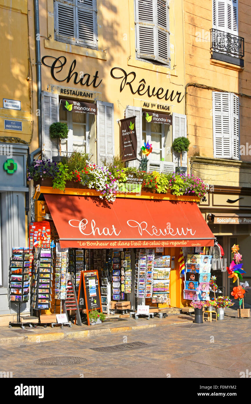 Shopfront con rack da cartolina sul marciapiede e ristorante sopra in un angolo della Place de l'Hotel de Ville in Aix en Provence Sud della Francia Foto Stock