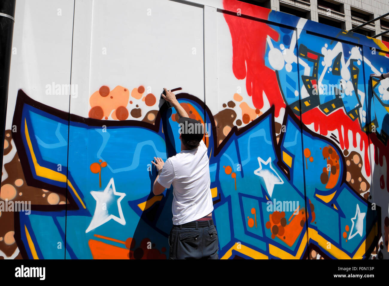 Uomo di verniciatura a spruzzo di graffiti su Great Eastern Street palizzata in Shoreditch, East London REGNO UNITO KATHY DEWITT Foto Stock