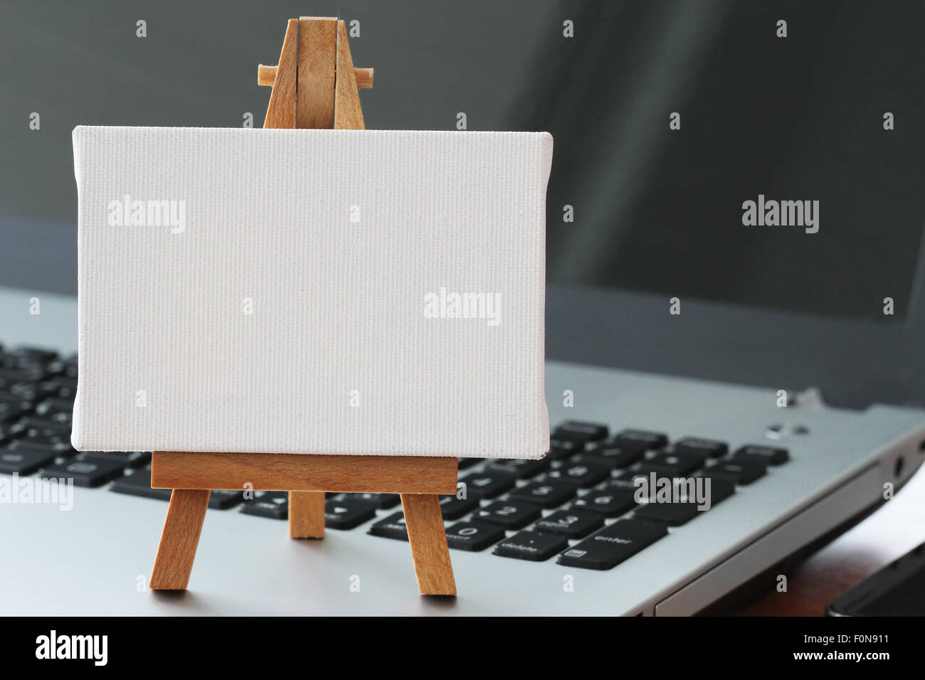 Tela vuota e il cavalletto in legno sul computer portatile come concetto Foto Stock