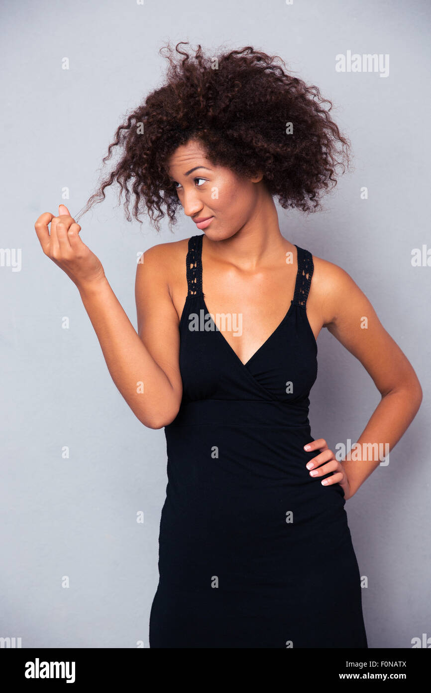 Ritratto di afro american donna in abito nero di toccare i suoi capelli su sfondo grigio Foto Stock