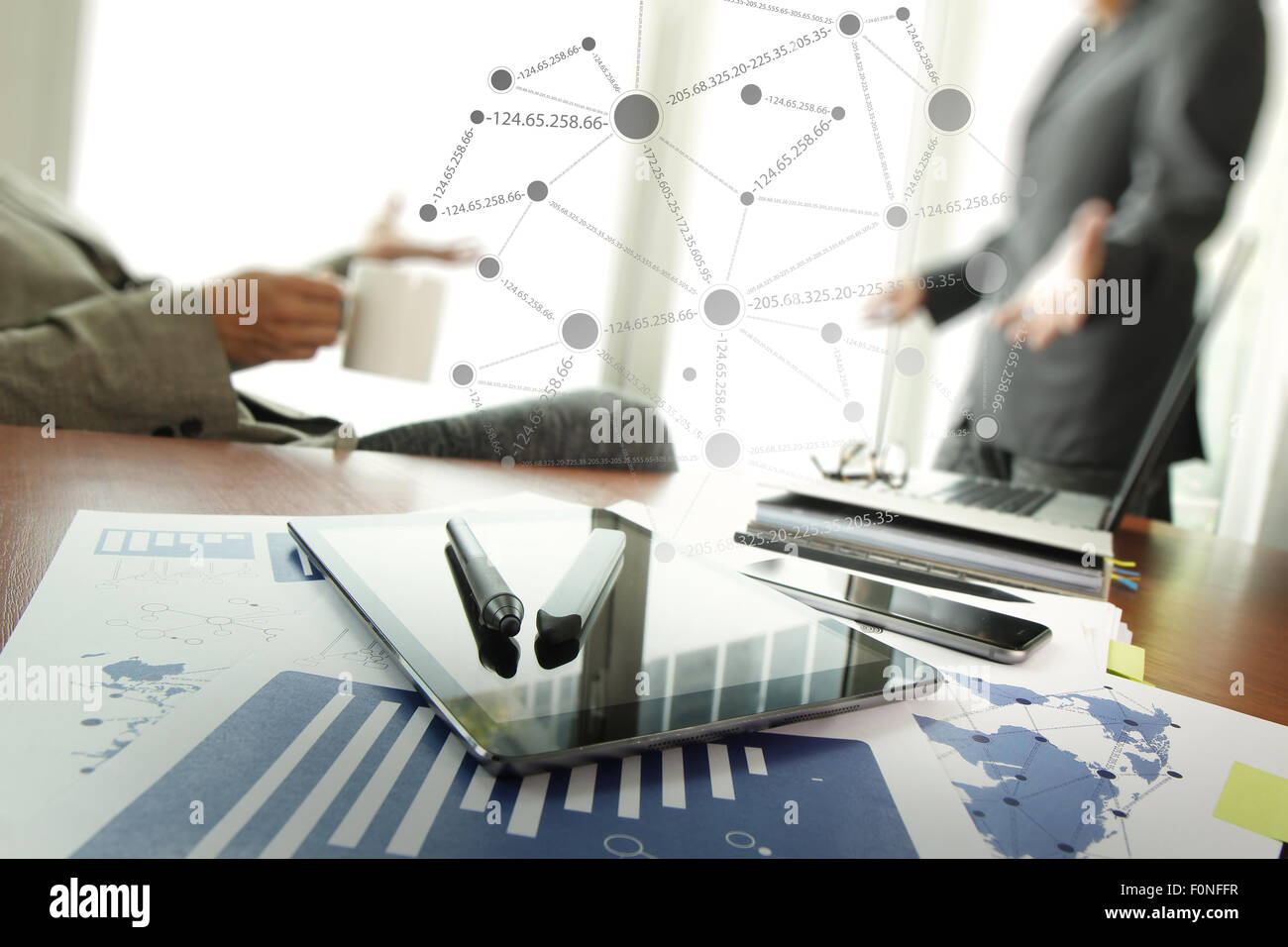 Documenti aziendali su office tabella con smart phone e laptop e due colleghi per discutere i dati in background Foto Stock