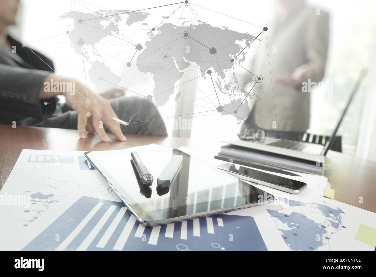Documenti aziendali su office tabella con smart phone e laptop e due colleghi per discutere i dati in background Foto Stock