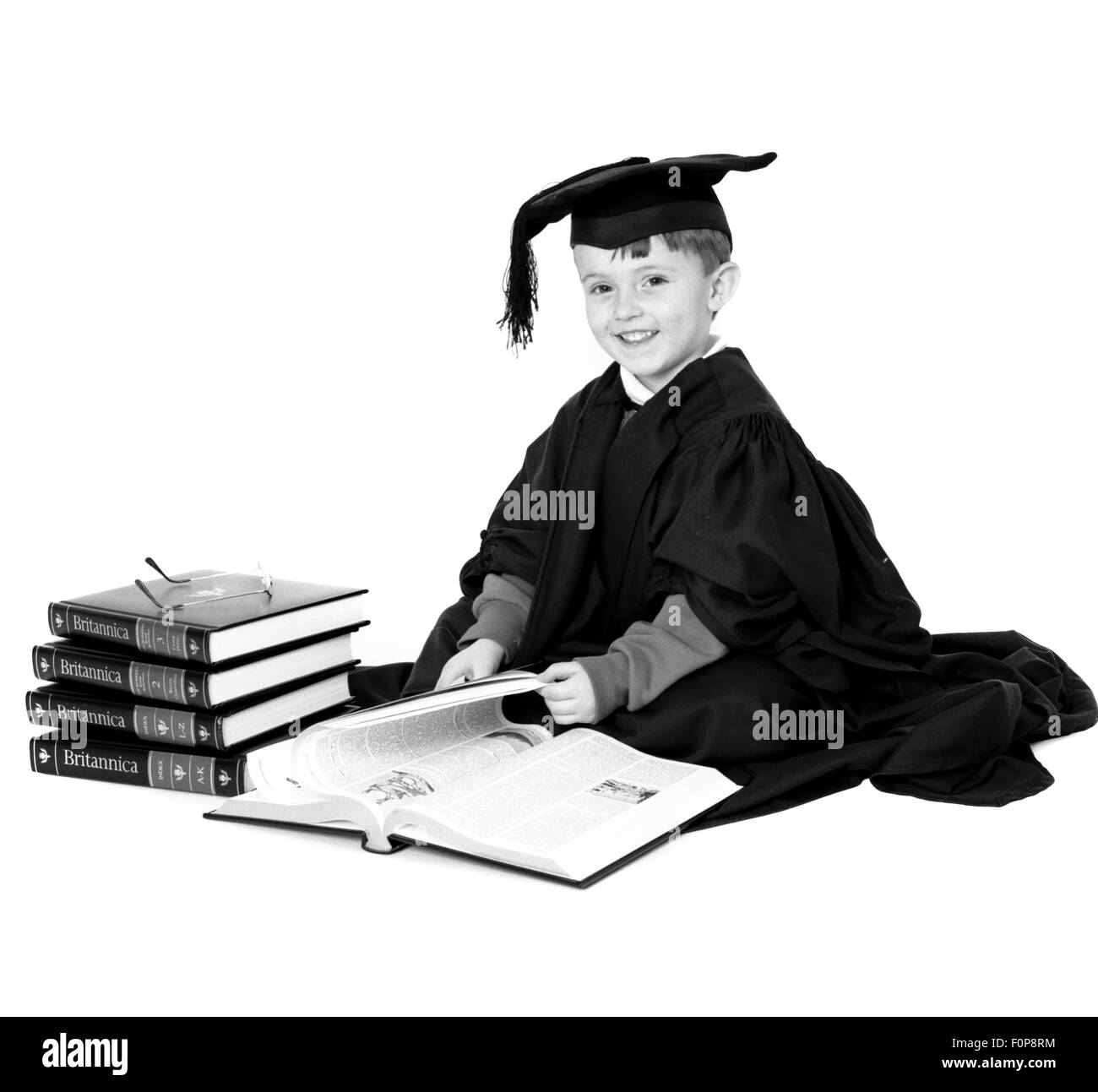 Ragazzo giovane vestito in un mortaio board e camice lettura Enciclopedia Britannica Foto Stock