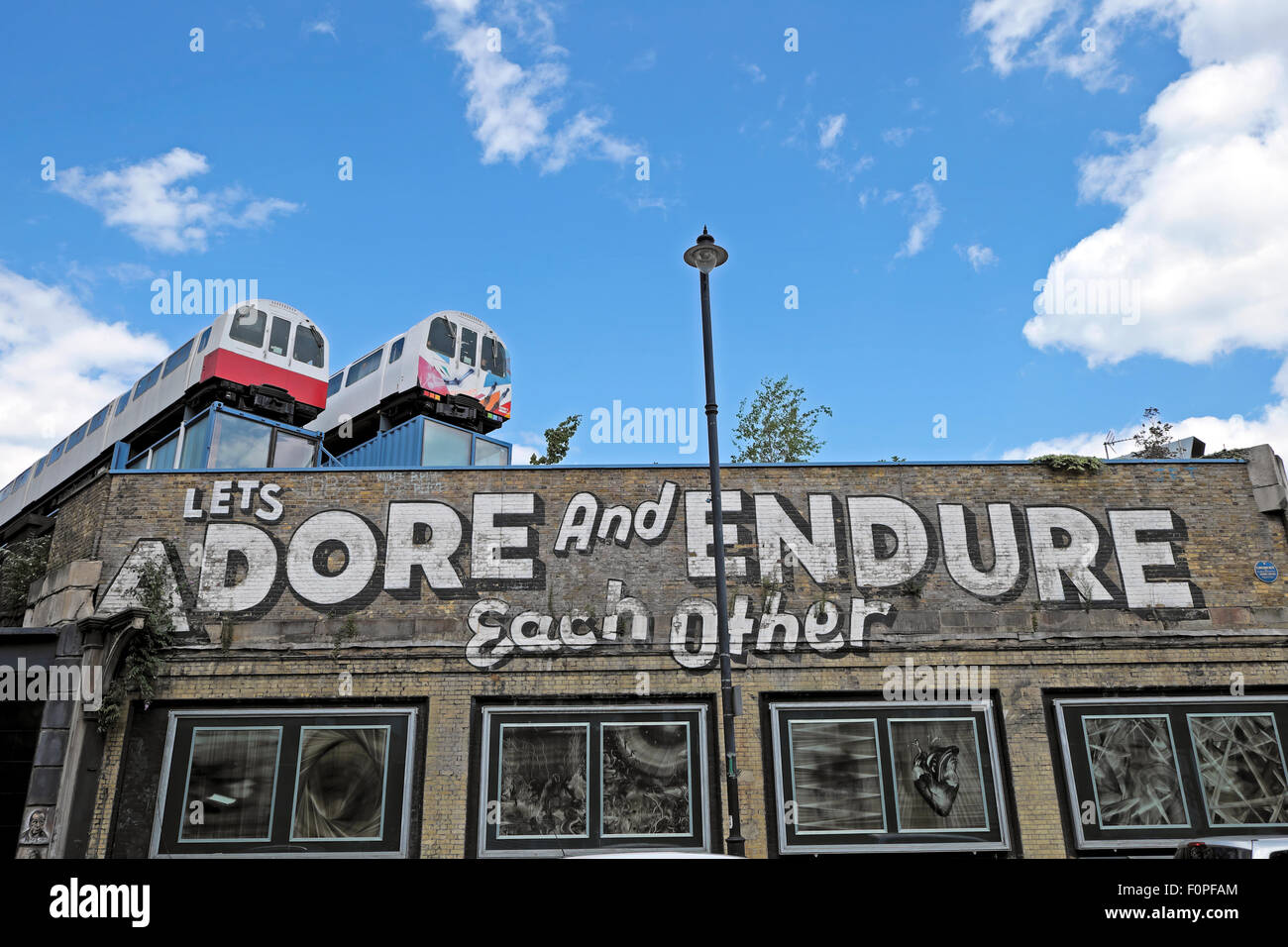 Cerchiamo di adorare e sopportare ogni altra graffiti sul muro con carrozze ferroviarie su un tetto Great Eastern Street in Shoreditch East London REGNO UNITO KATHY DEWITT Foto Stock