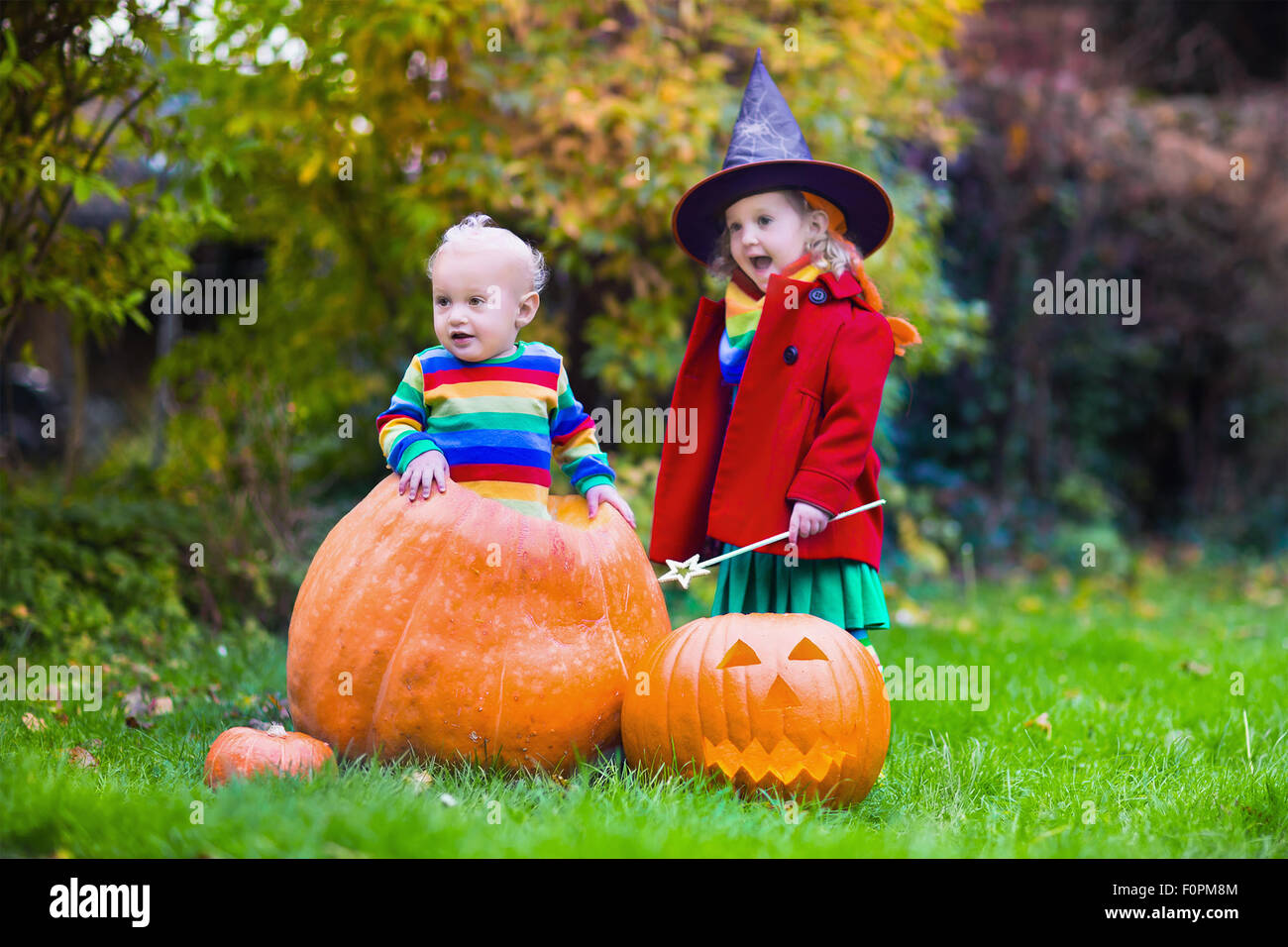 Bambina in costume da strega e baby boy in zucca enorme giocando in autunno park. I bambini di Halloween dolcetto o scherzetto. Foto Stock