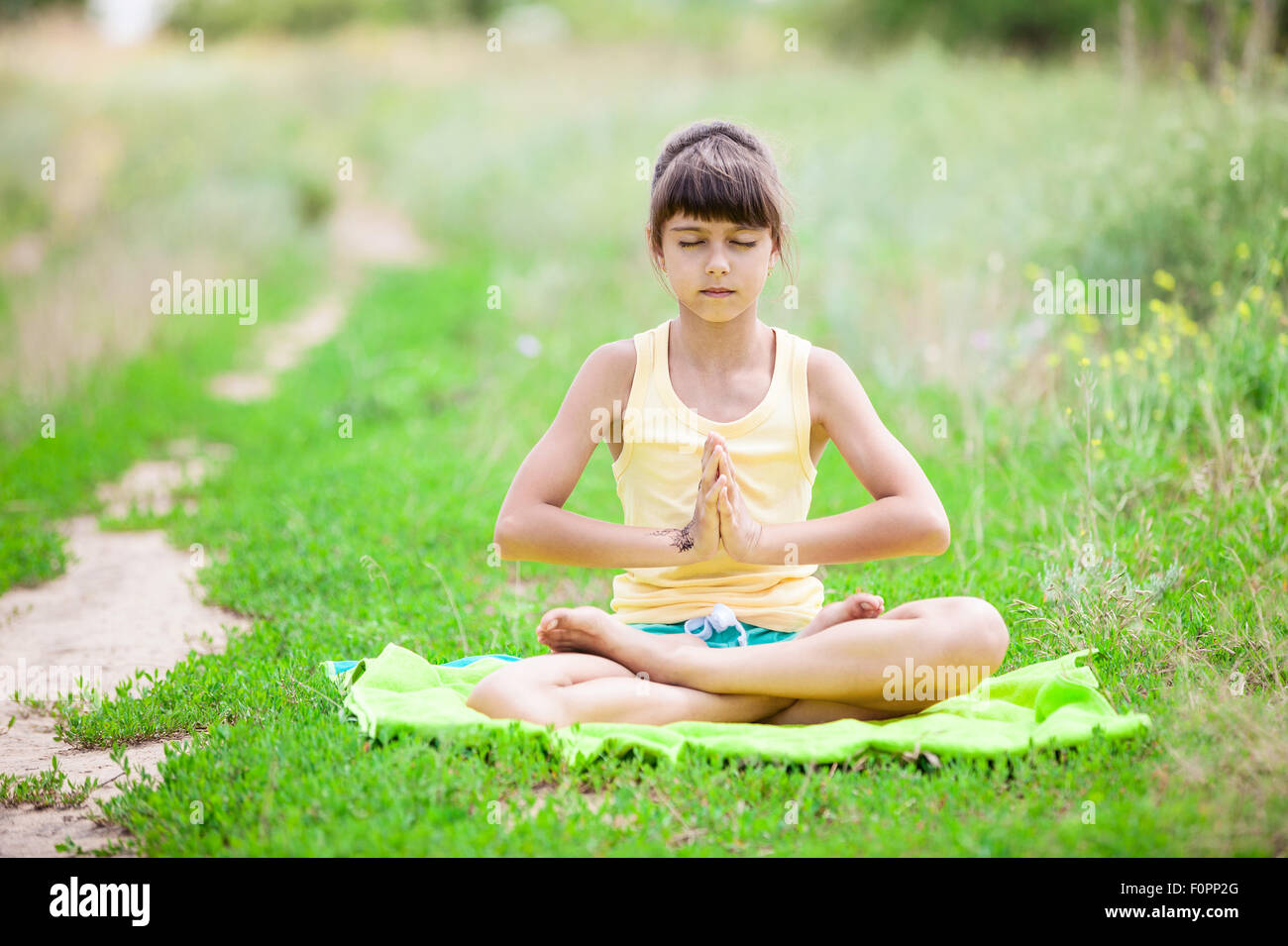 Piccola ragazza rilassante mentre è seduto nella posizione del loto sull'erba. Foto Stock