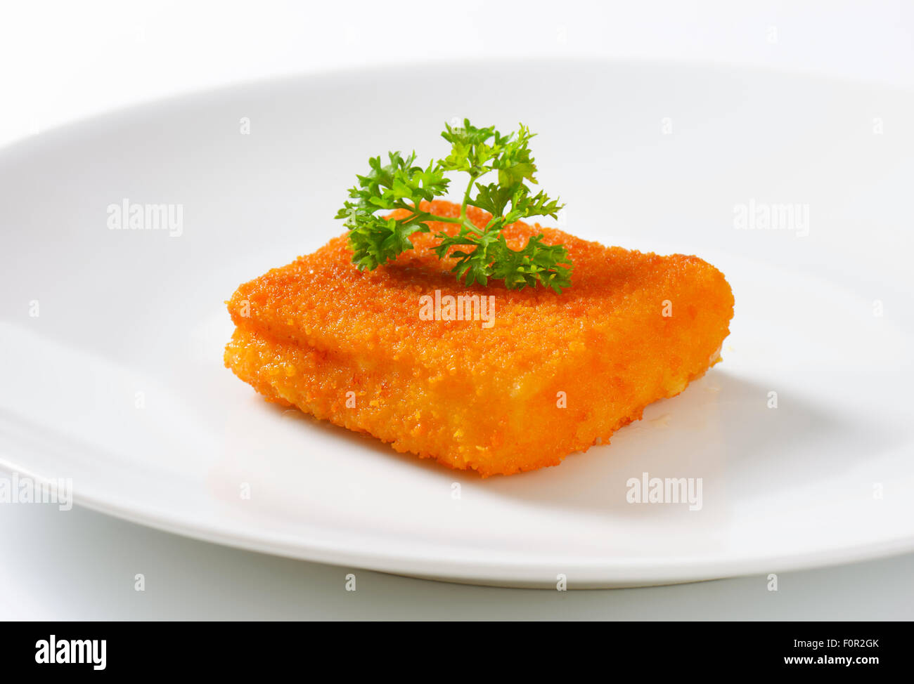 Pezzo di pesce fritto con prezzemolo fresco sulla piastra bianca Foto Stock