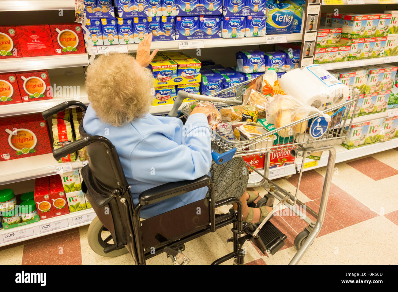 Signora anziana nel suo degli anni novanta con clip-sulla sedia a rotelle carrello shopping nel supermercato Tesco. In Inghilterra. Regno Unito Foto Stock
