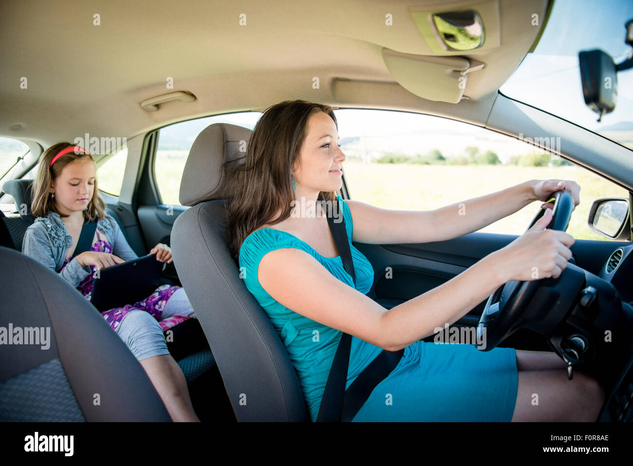 Madre di guida e auto bambino seduto sul sedile posteriore e giocare con il tablet Foto Stock