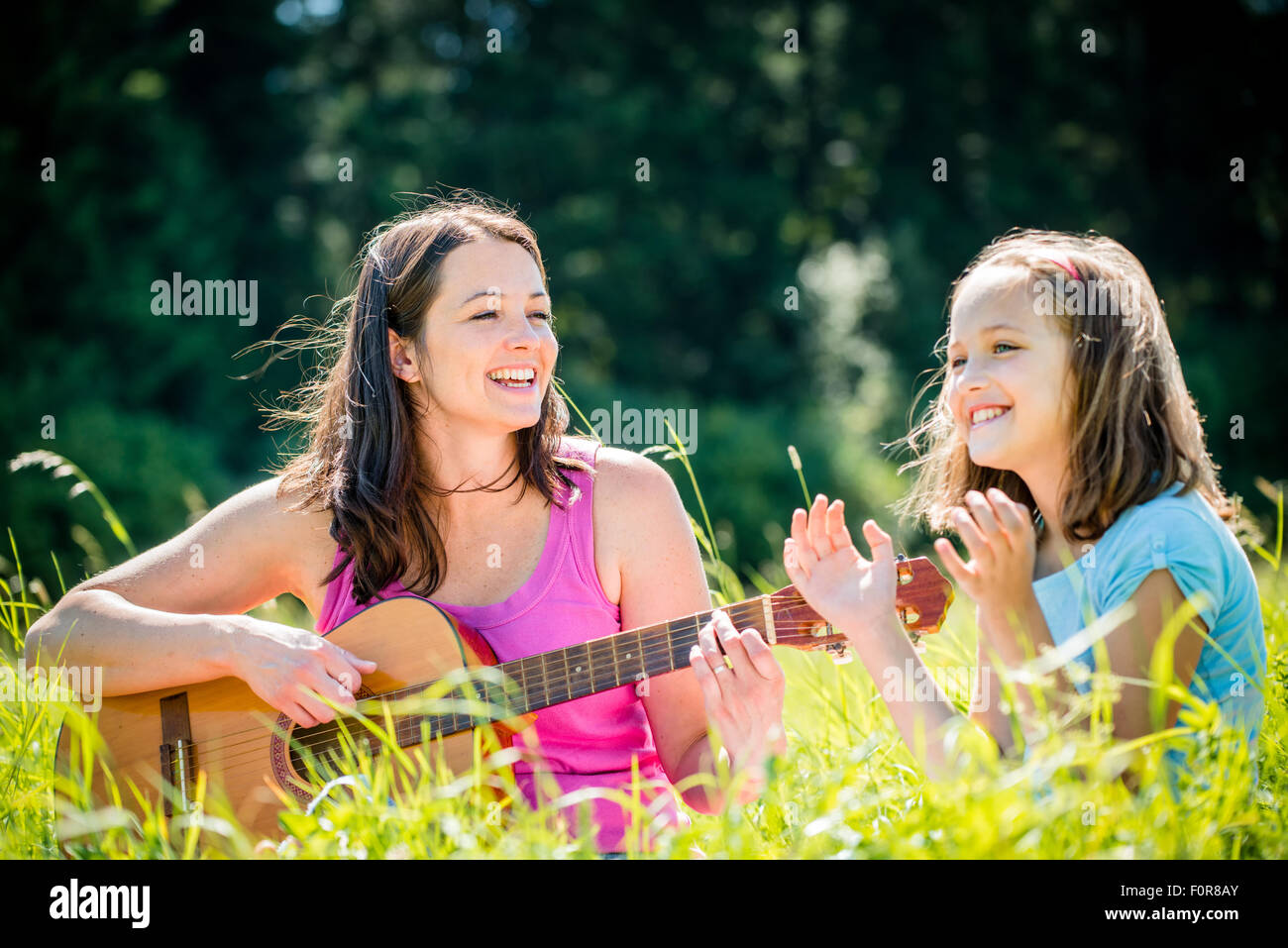 La donna a suonare la chitarra al suo bambino outdoor in natura sulla giornata di sole Foto Stock
