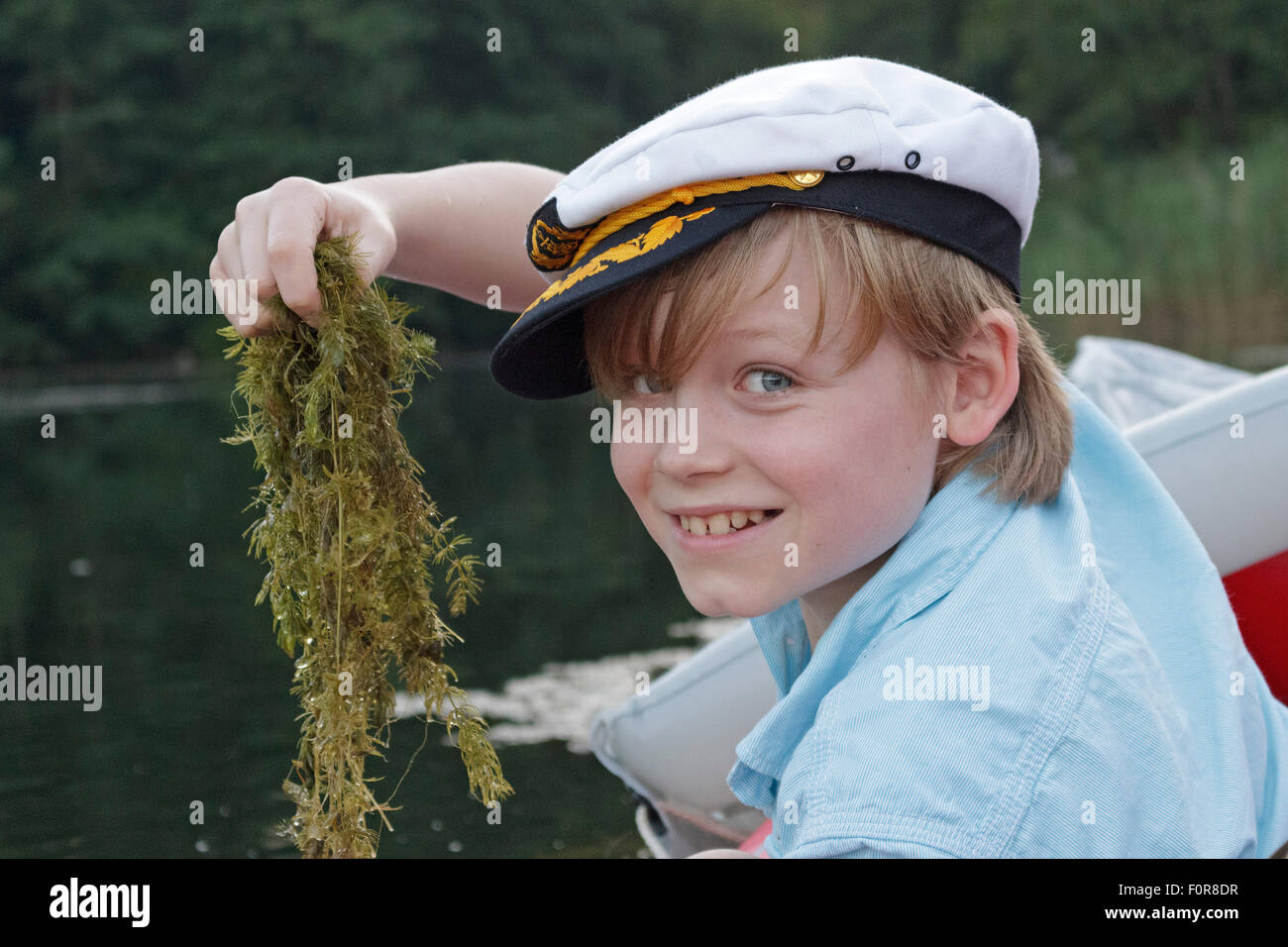 Ragazzo con il capitano del cappello tenendo su alghe di un lago Foto Stock