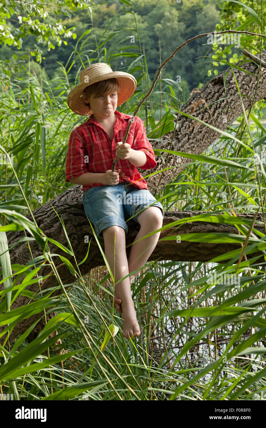Ragazzo giovane vestito come Huckleberry Finn seduta di pesca in una  struttura ad albero Foto stock - Alamy