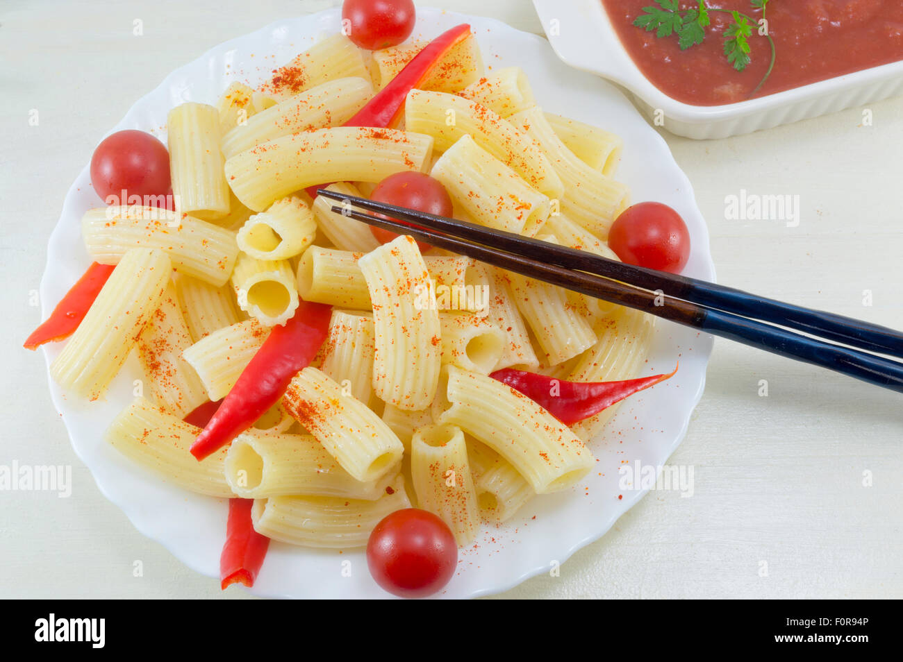 Pasta con pomodori ciliegia e pepe rosso servito con una salsa di pomodoro in un arco bianco pronto per mangiare con le bacchette in Asia Foto Stock