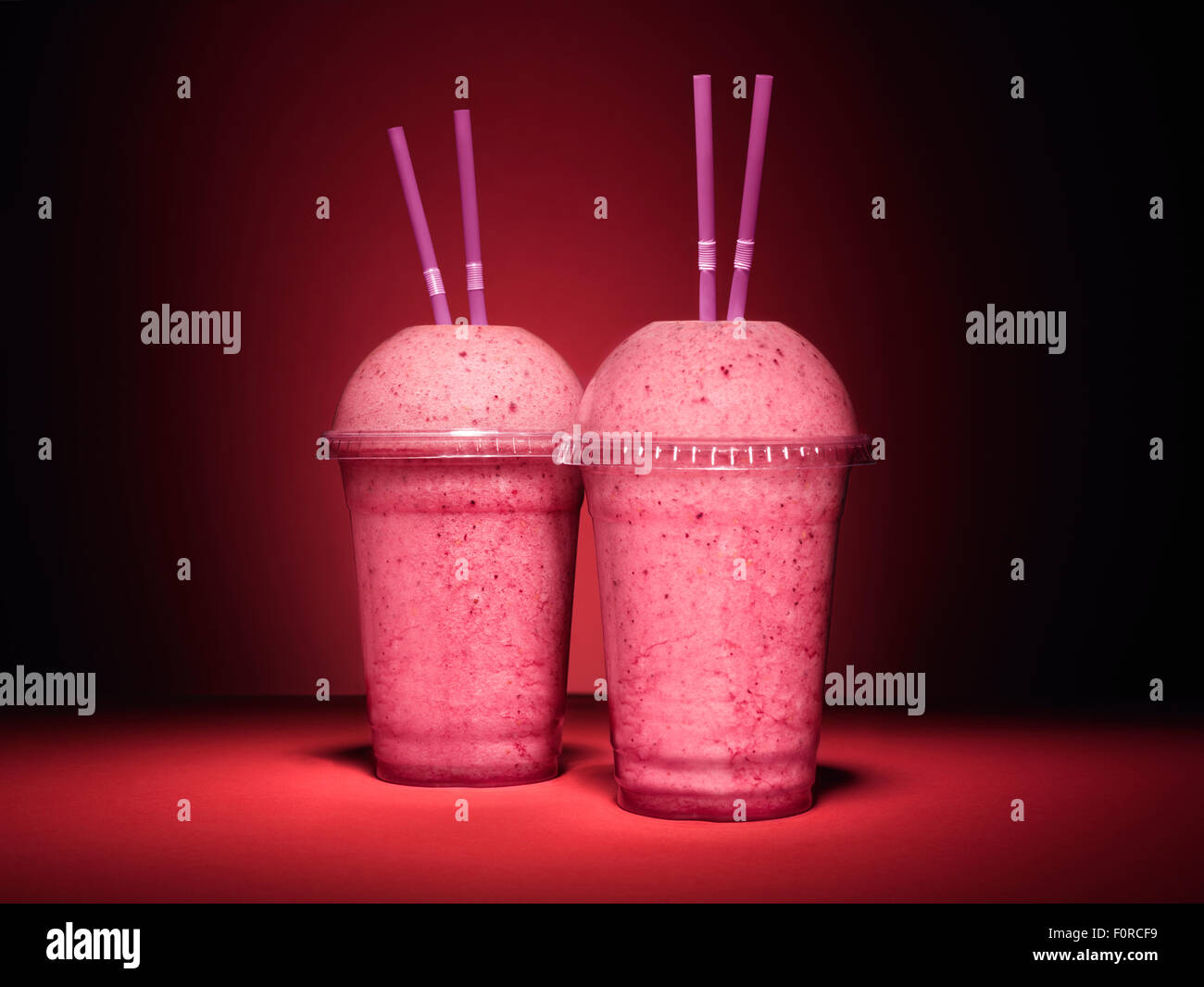 Colpo di una coppia di rosa, frutta, berry smoothie su una vivace sfondo rosso con copia spazio per il progettista. Foto Stock