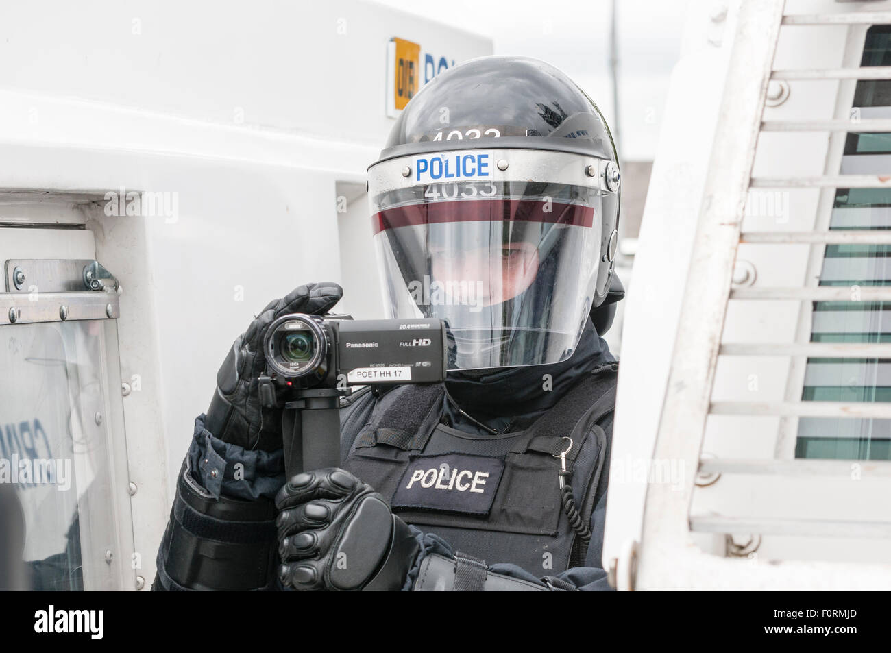 Un PSNI funzionario di polizia vestito in uniforme di tumulto utilizza una videocamera per raccogliere prove durante un disordine pubblico riot Foto Stock