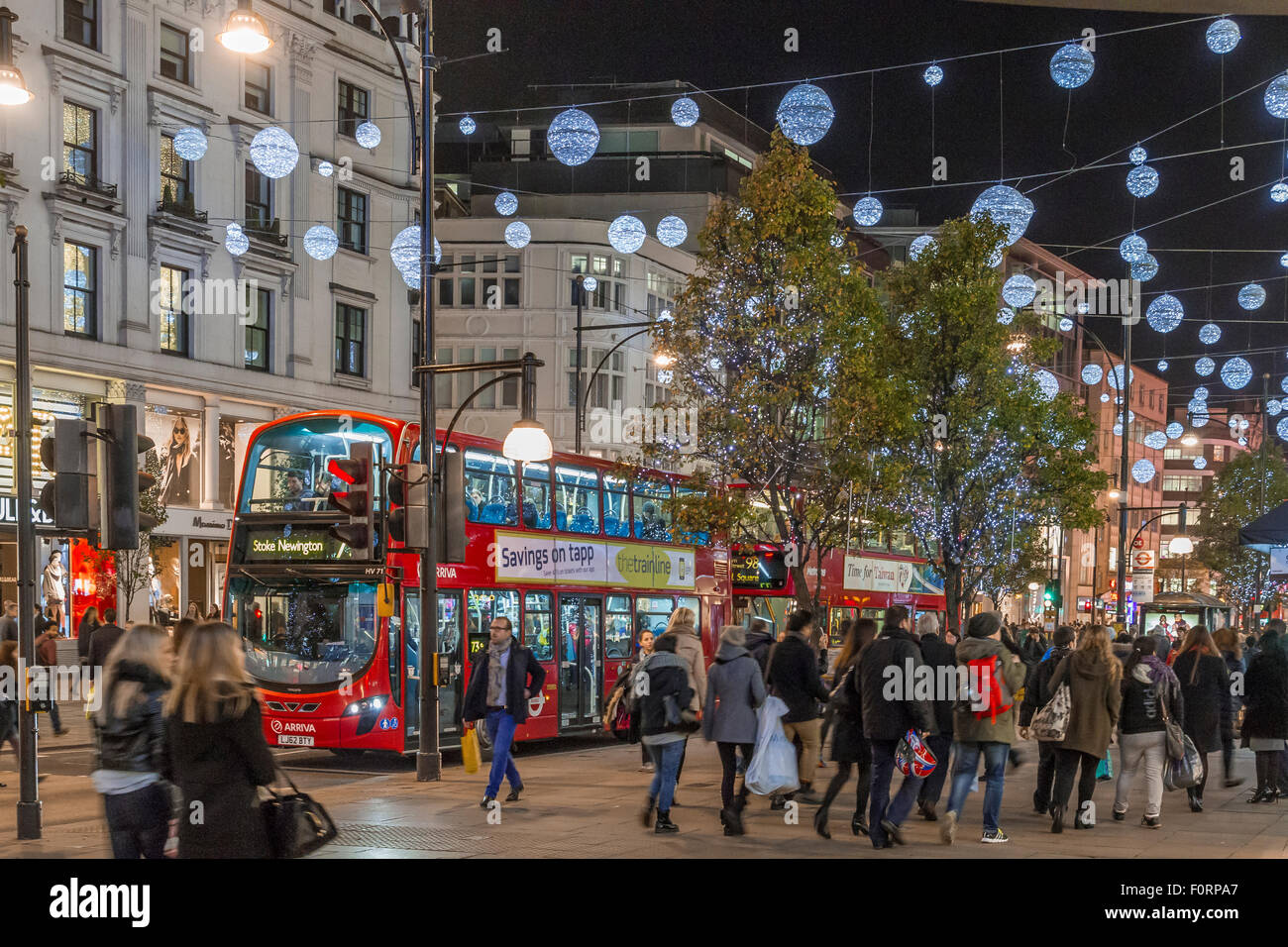 Gli autobus passano sotto le luci di Natale su Oxford Street, frequentati da amanti dello shopping natalizio, a Natale, Oxford Street, Londra, Regno Unito Foto Stock