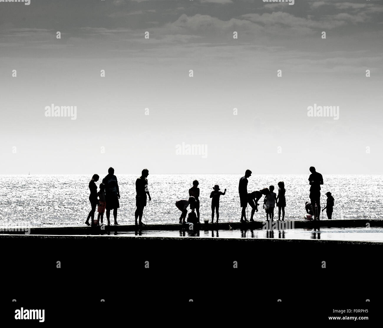 La silhouette di vacanzieri in piedi sul bordo della maree piscinetta per bambini in Viking Bay, Broadstairs Kent. Foto Stock