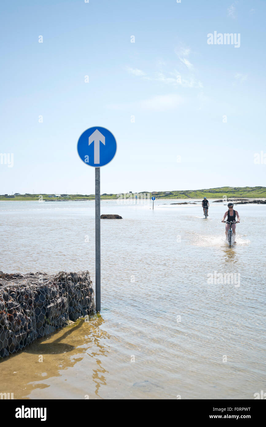 I ciclisti sulla spiaggia allagata percorso da Omey Island a marea alta Foto Stock
