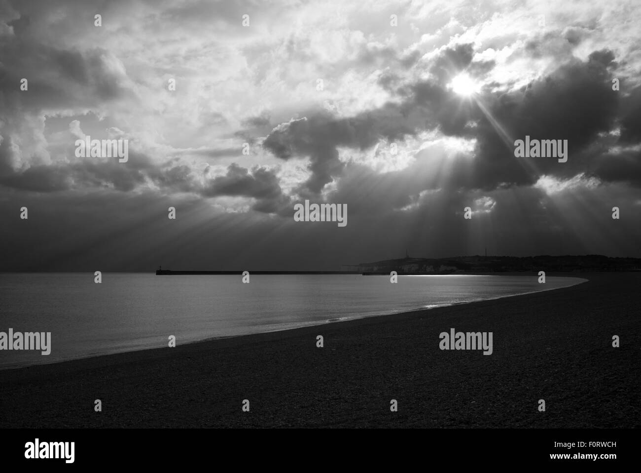 Raggi Suns attraverso il cloud oltre il mare calmo e la spiaggia vuota,Seaford, Sussex,nero e bianco Foto Stock