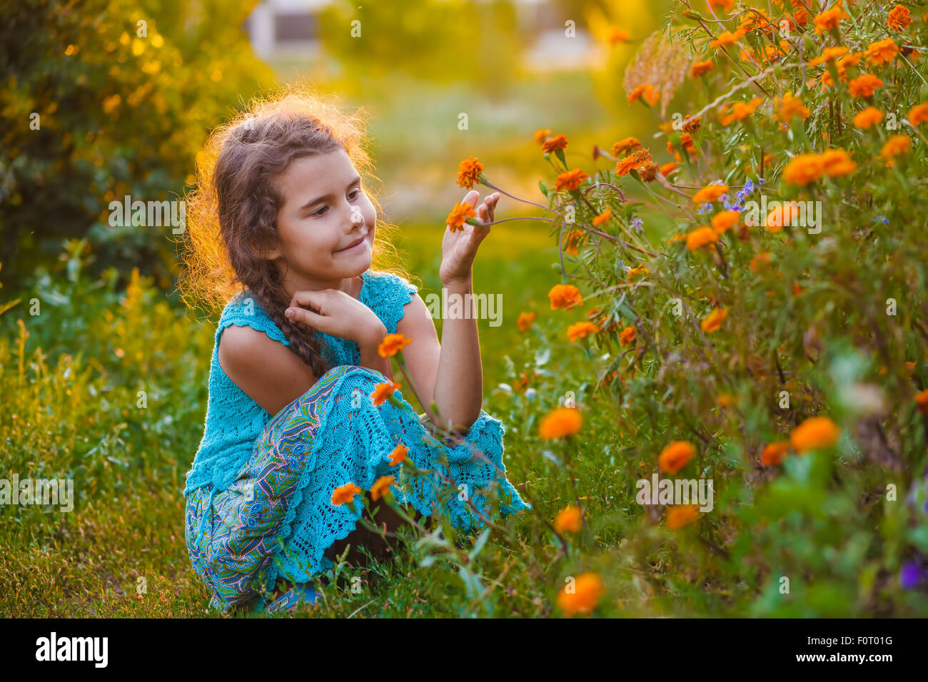 Teen ragazza seduta sul suo haunches e toccando fiore di arancia in Foto Stock