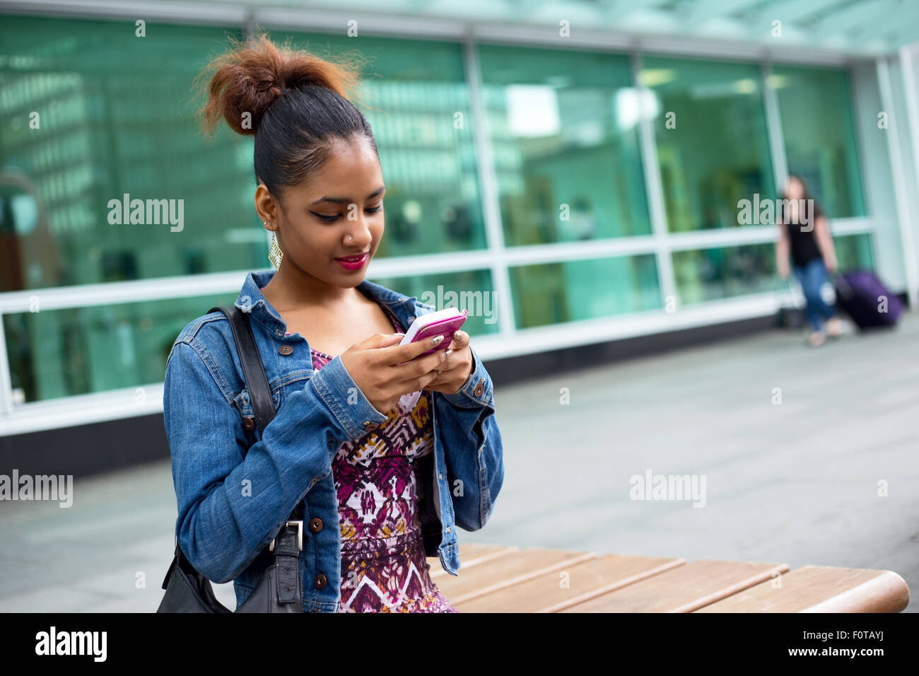 Giovane donna seduta su una panchina di inviare un messaggio di testo Foto Stock