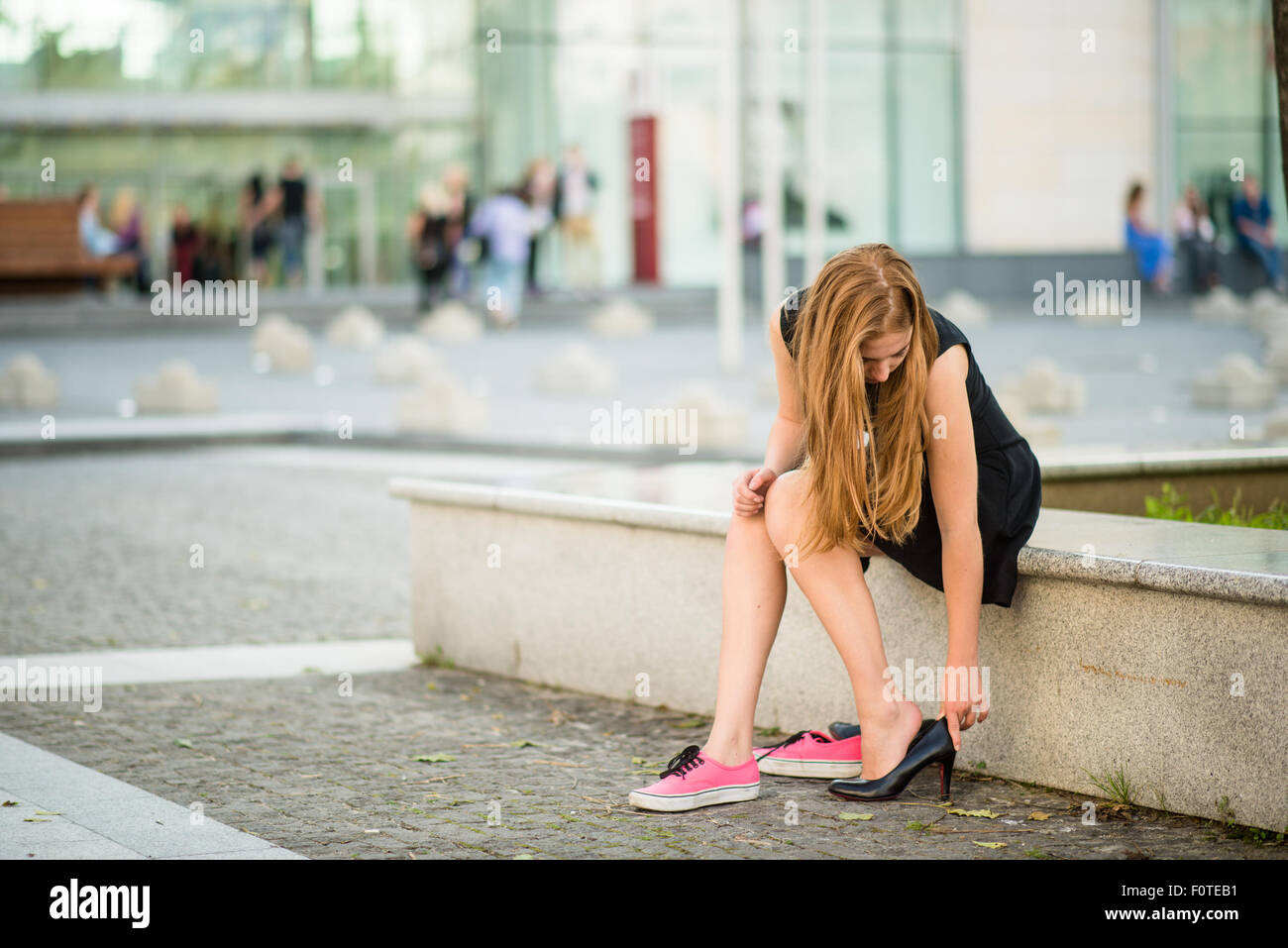 Giovane donna scarpe modifiche su via tacchi alti invece di sneakers Foto Stock