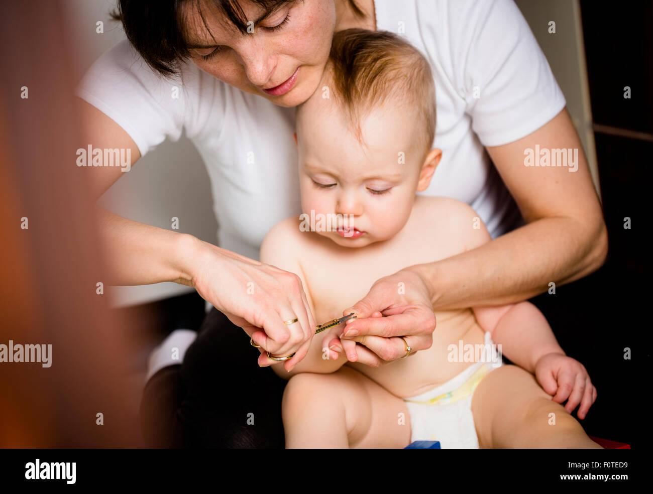 Madre il taglio di unghie delle mani del suo bambino - seduta sul pavimento nel bagno Foto Stock