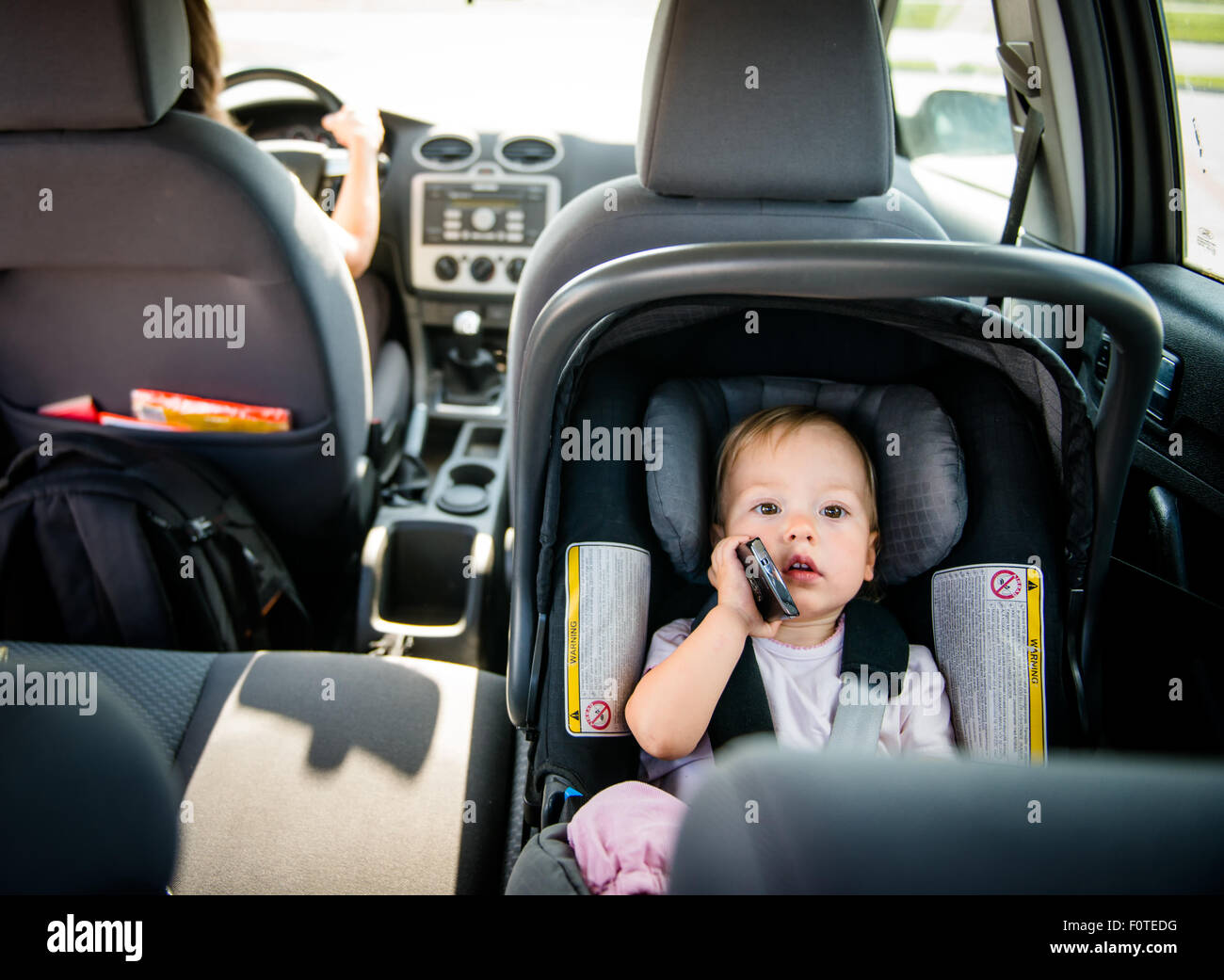 Madre di guida e auto bambino seduto sul sedile posteriore e giocare con il telefono cellulare Foto Stock