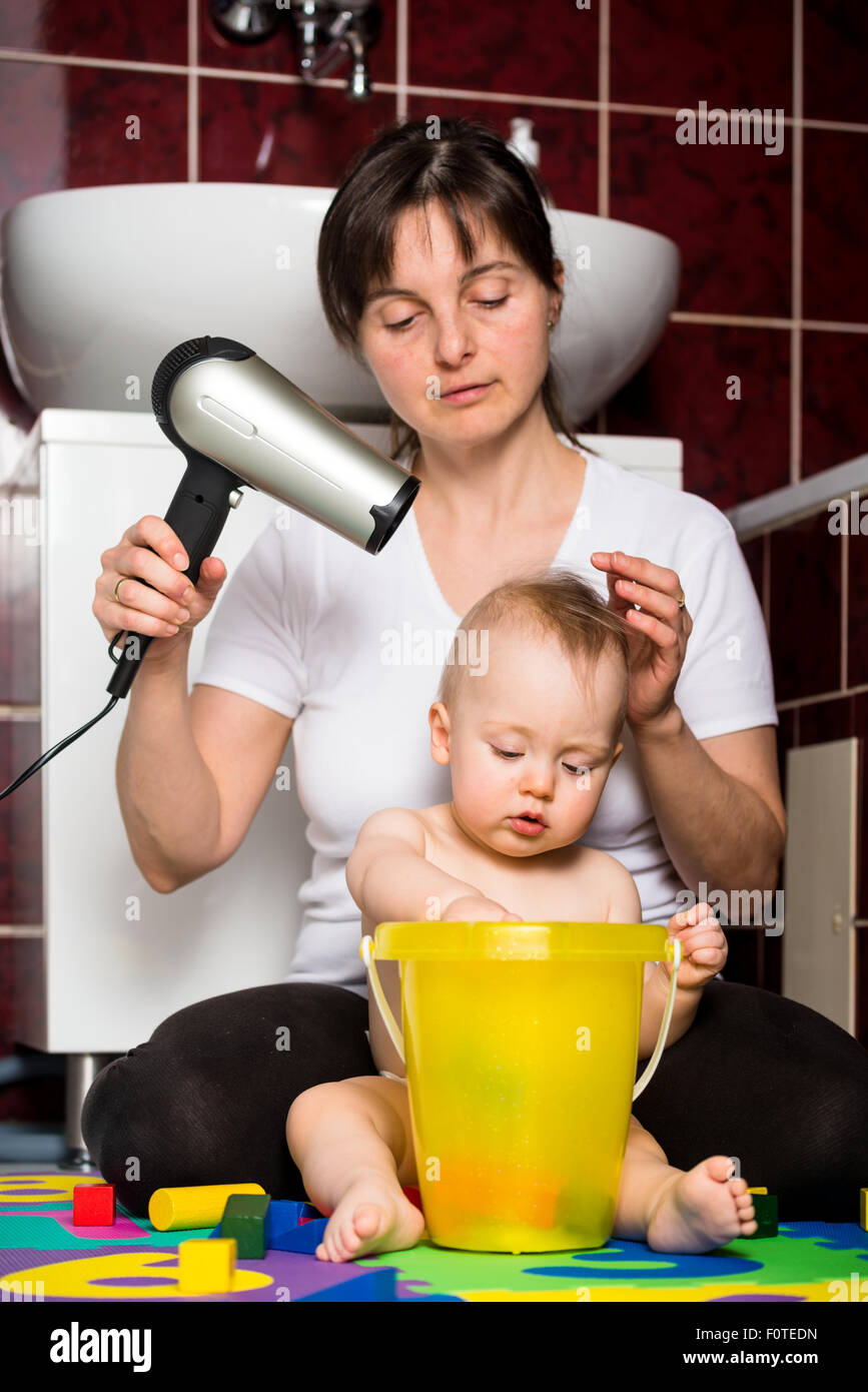 Madre l'asciugatura dei capelli del suo bambino mentre il bambino sta giocando con i giocattoli Foto Stock