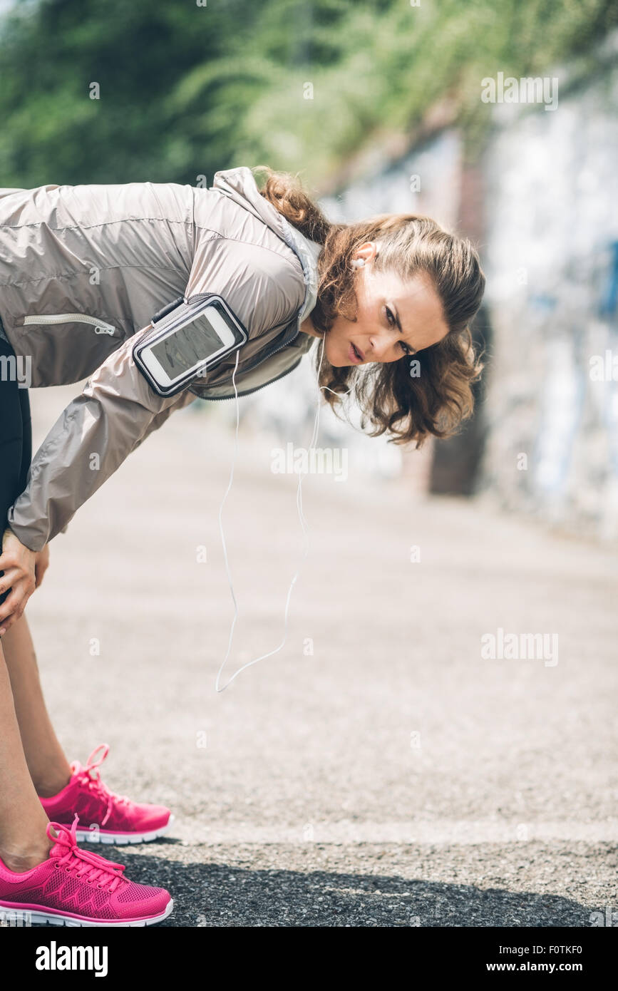 Un atletico donna si appoggia al di sopra e le mani sulle sue ginocchia e distende le sue gambe dopo una lunga corsa. Sul suo braccio, indossa il suo devic Foto Stock