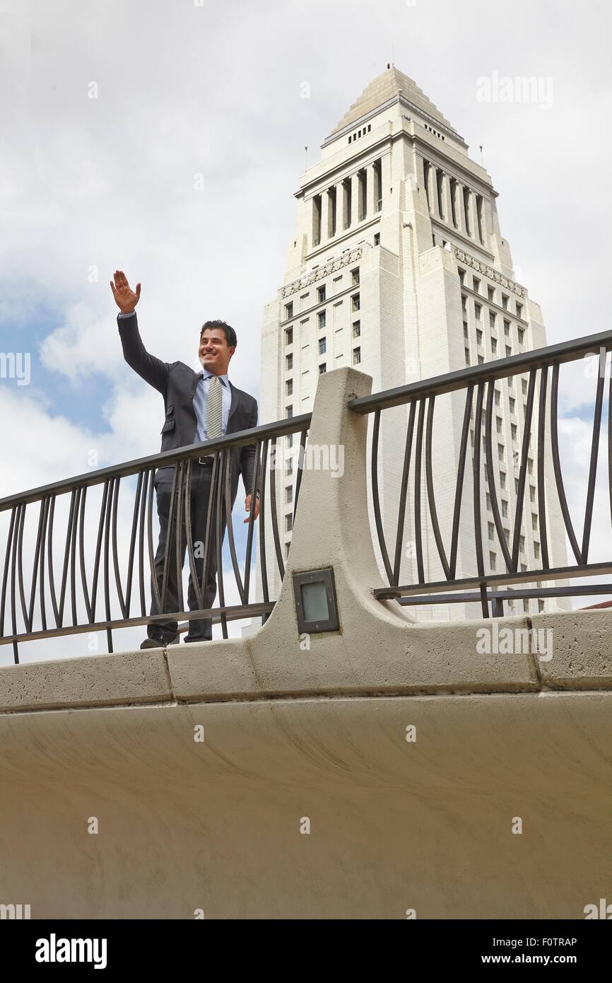 Business man in piedi sul marciapiede, agitando, sorridente, Los Angeles City Hall, CALIFORNIA, STATI UNITI D'AMERICA Foto Stock