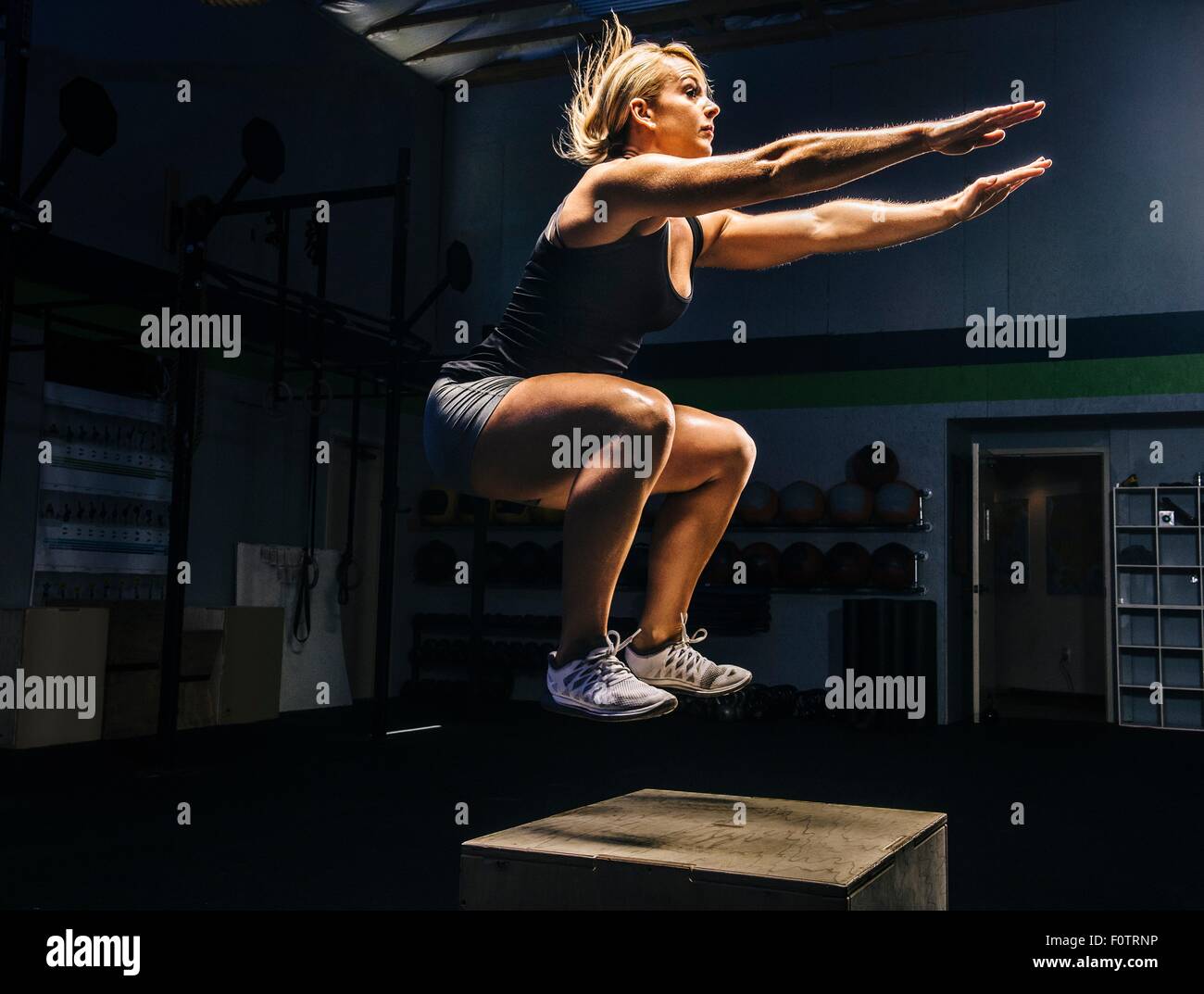 Giovane donna jumping metà aria sulla scatola di palestra con bracci raggiungendo fuori Foto Stock