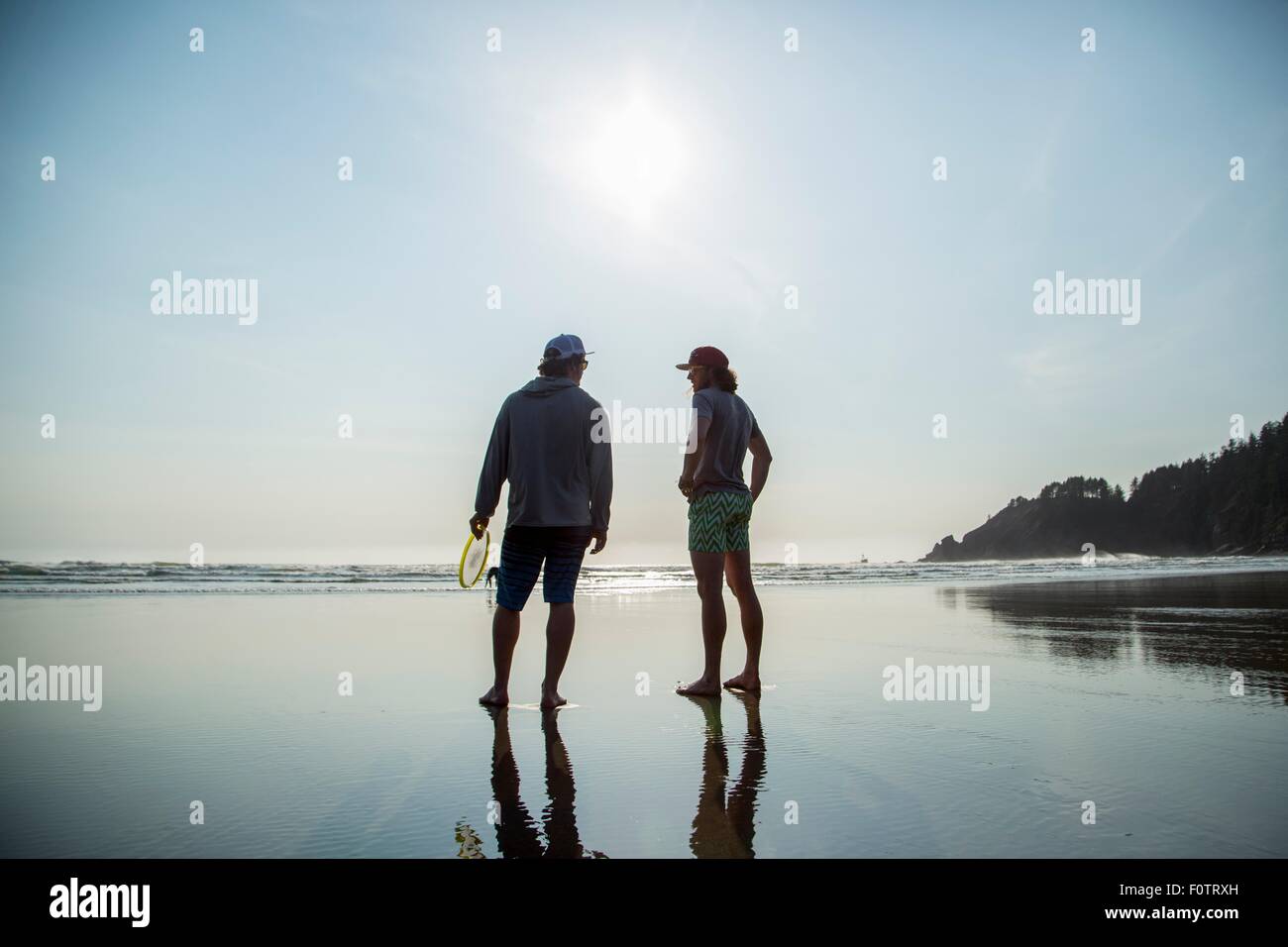 Stagliano posteriore vista di due giovani uomini in chat su brevi Sands Beach, Oregon, Stati Uniti d'America Foto Stock