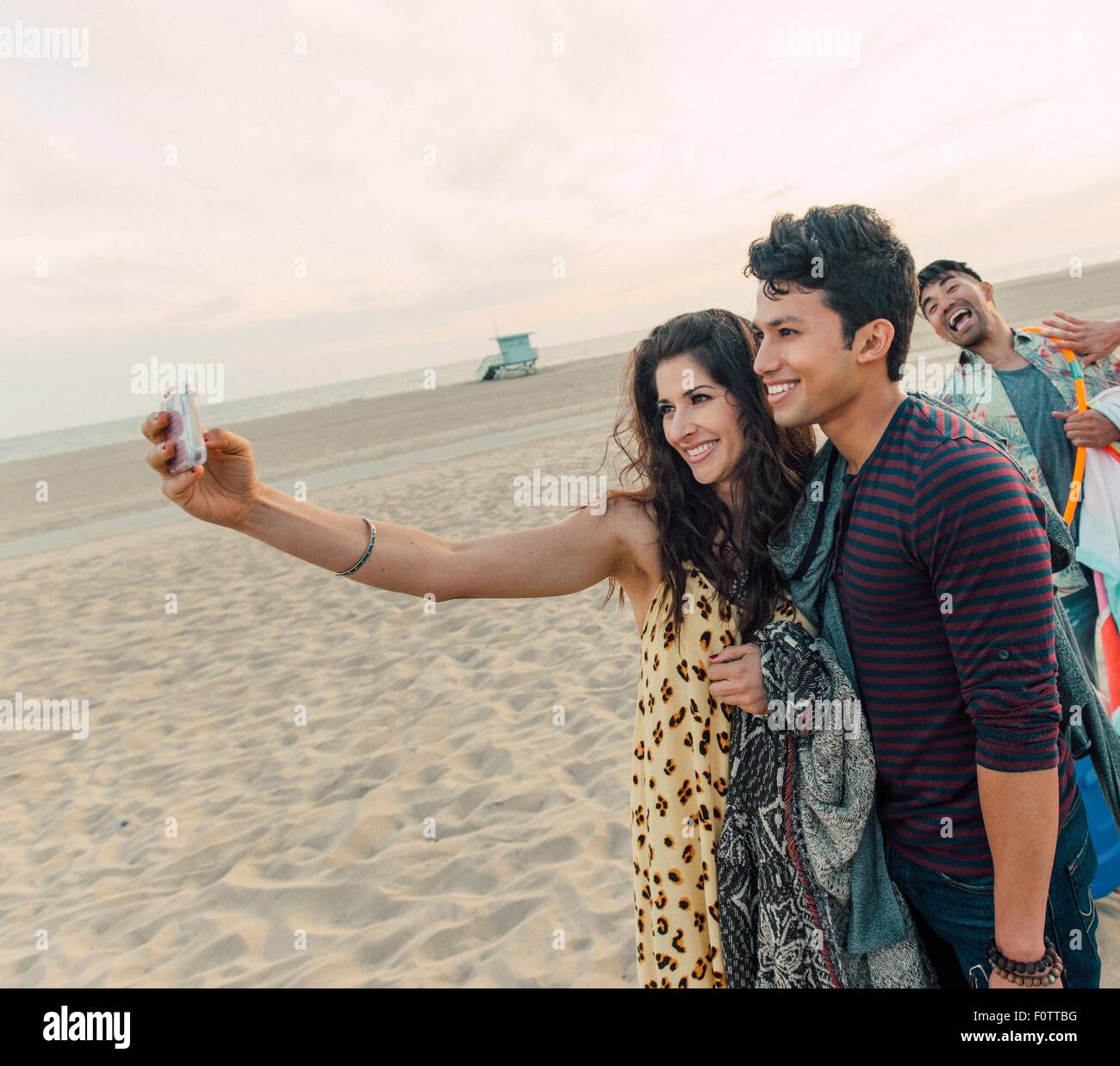 Gruppo di amici a piedi lungo la spiaggia, coppia giovane tenendo autoritratto con lo smartphone Foto Stock